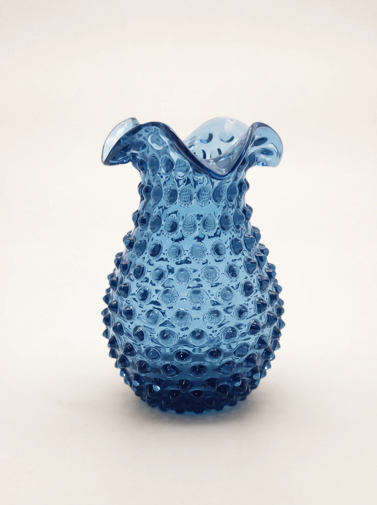 Translucent blue hobnail glass vase with a bulbous studded body and flared, ruffled rim