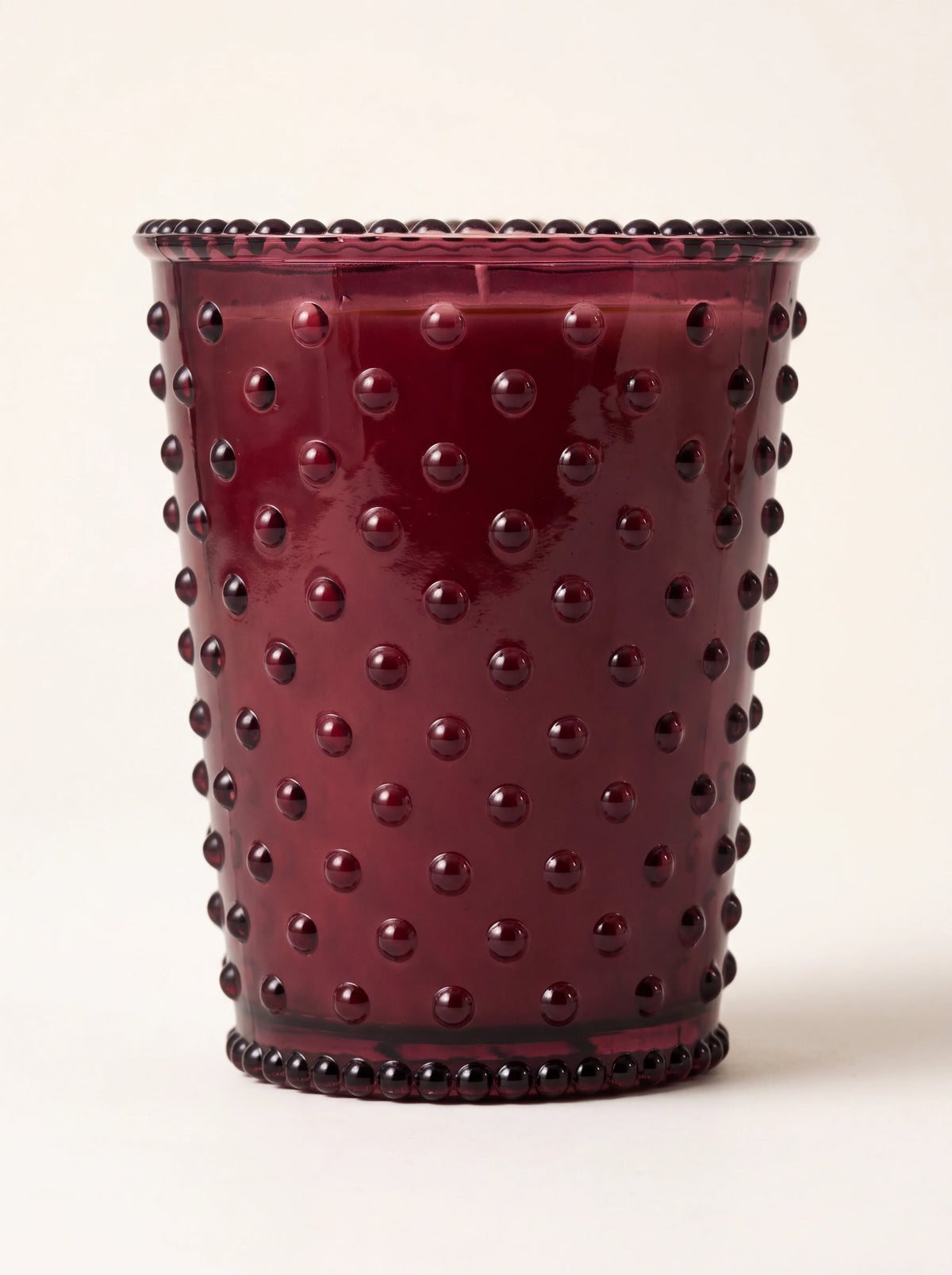 Scented candle in a cranberry red glass vessel with raised hobnail studs and beaded rims