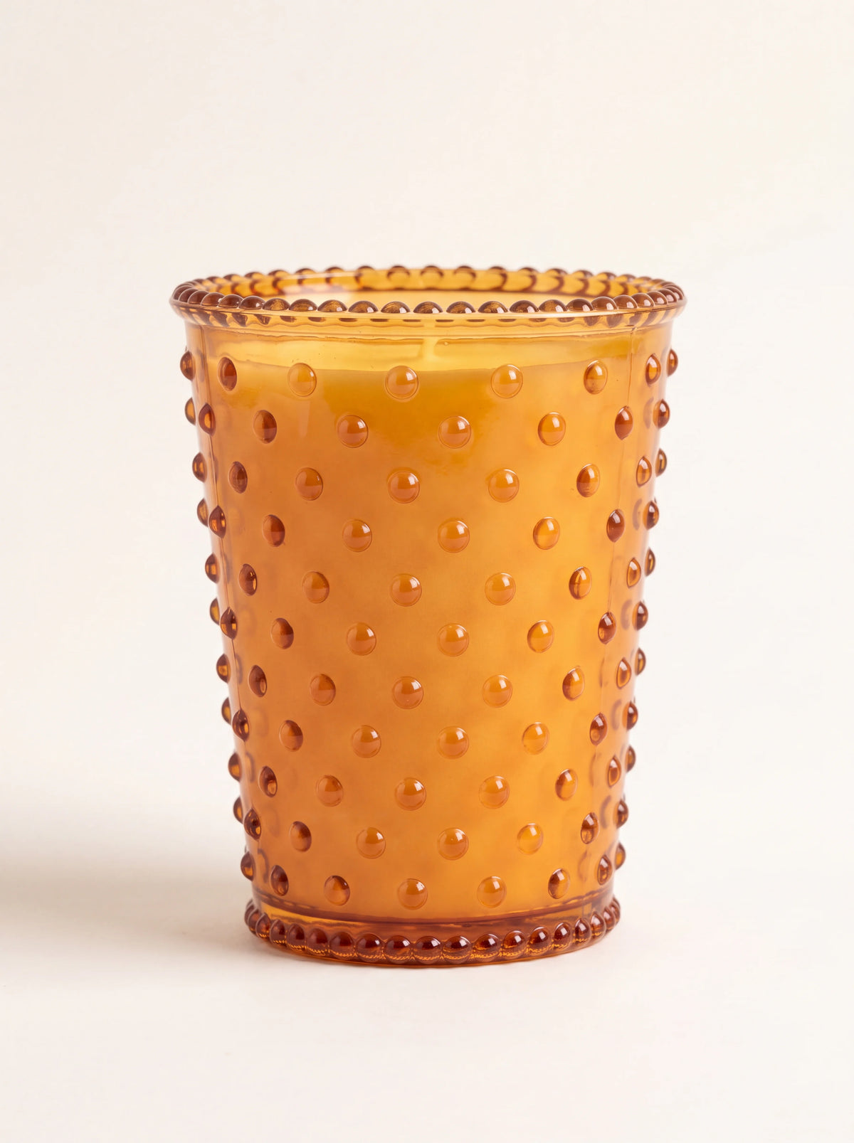 Scented candle in an amber hobnail glass vessel with raised studs and a beaded rim