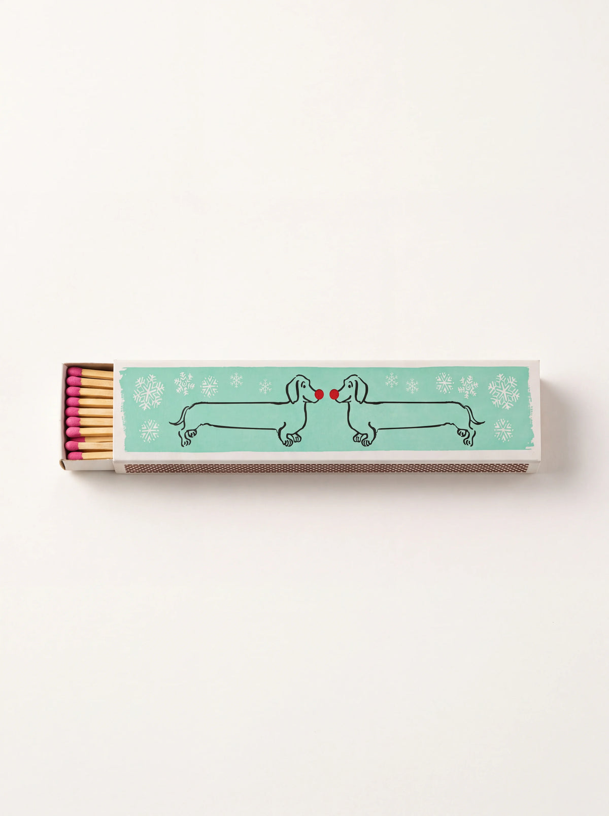 Long matchbox illustrated with two dachshunds and snowflakes on aqua, open to show pink-tipped matches