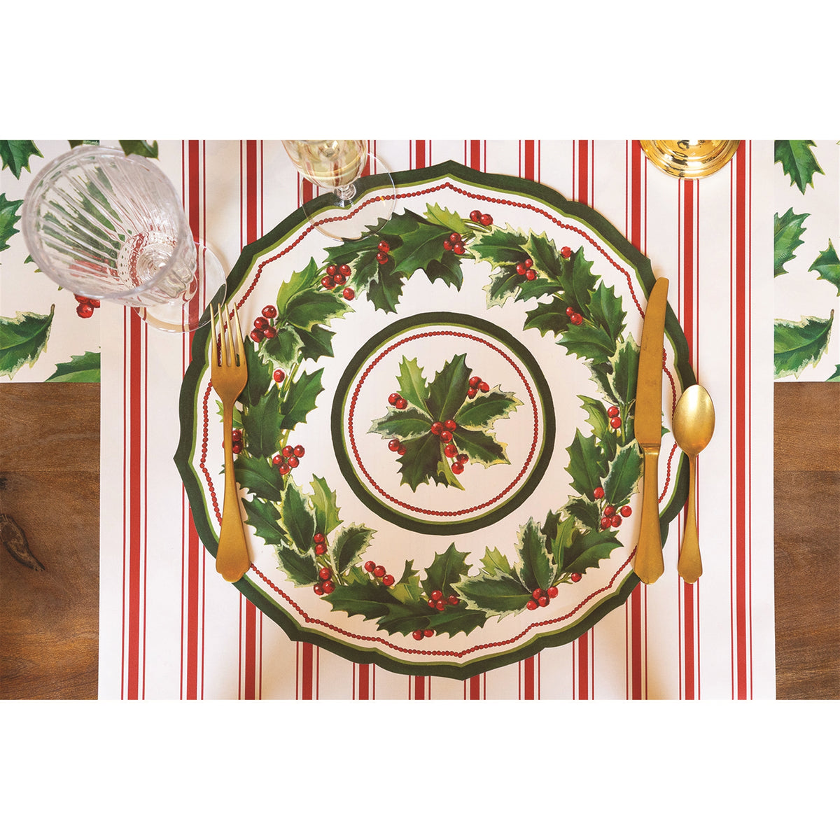 Holly paper placemat on a red-and-white striped runner, set with gold cutlery and a stemmed glass