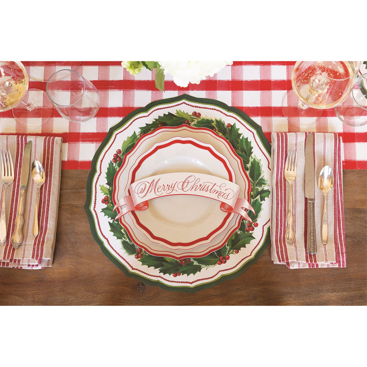 Holly paper placemat layered under plates with a banner reading Merry Christmas, on red gingham