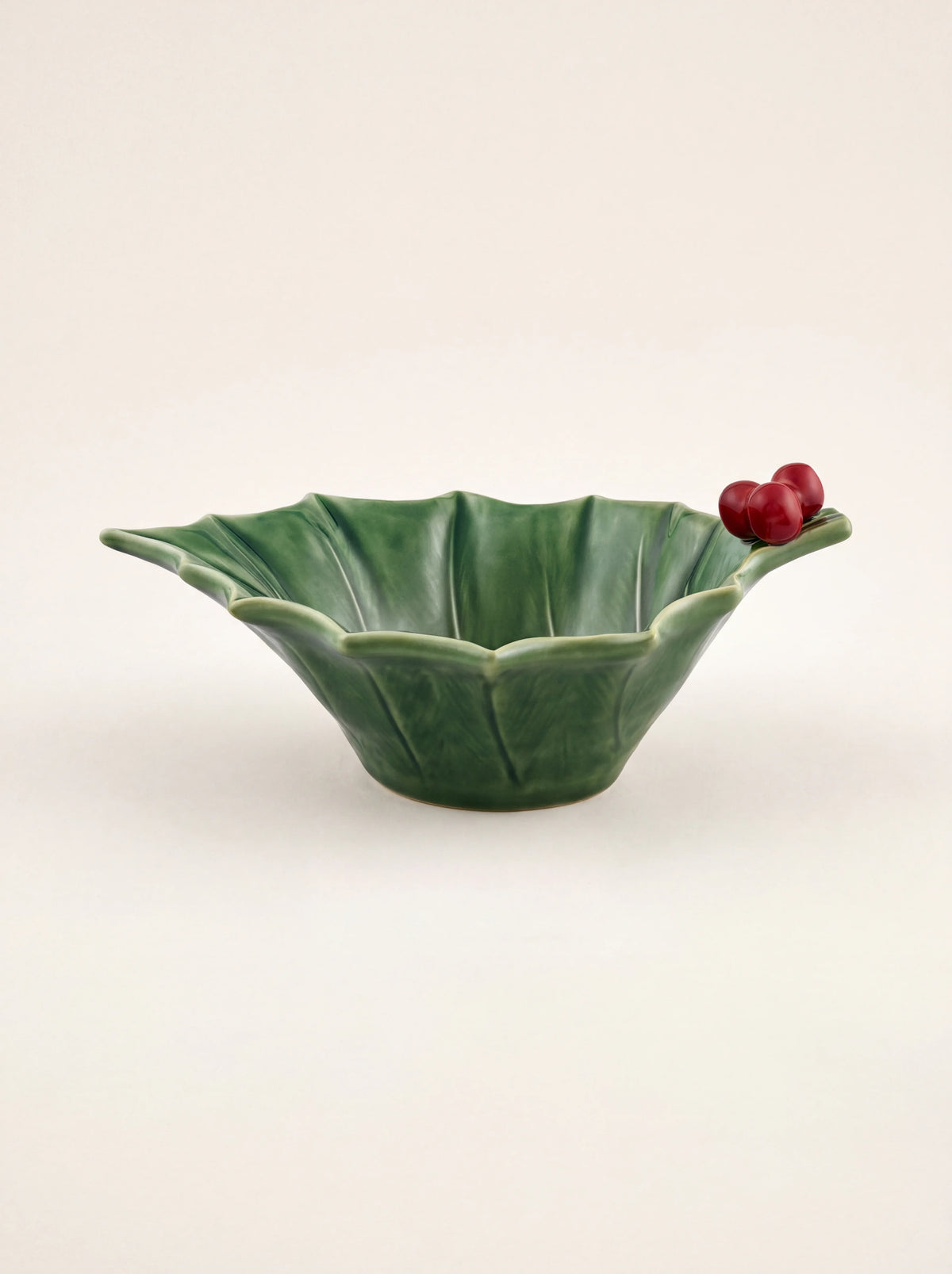 Green glazed earthenware bowl shaped like holly leaves with textured veining and red berries on the rim