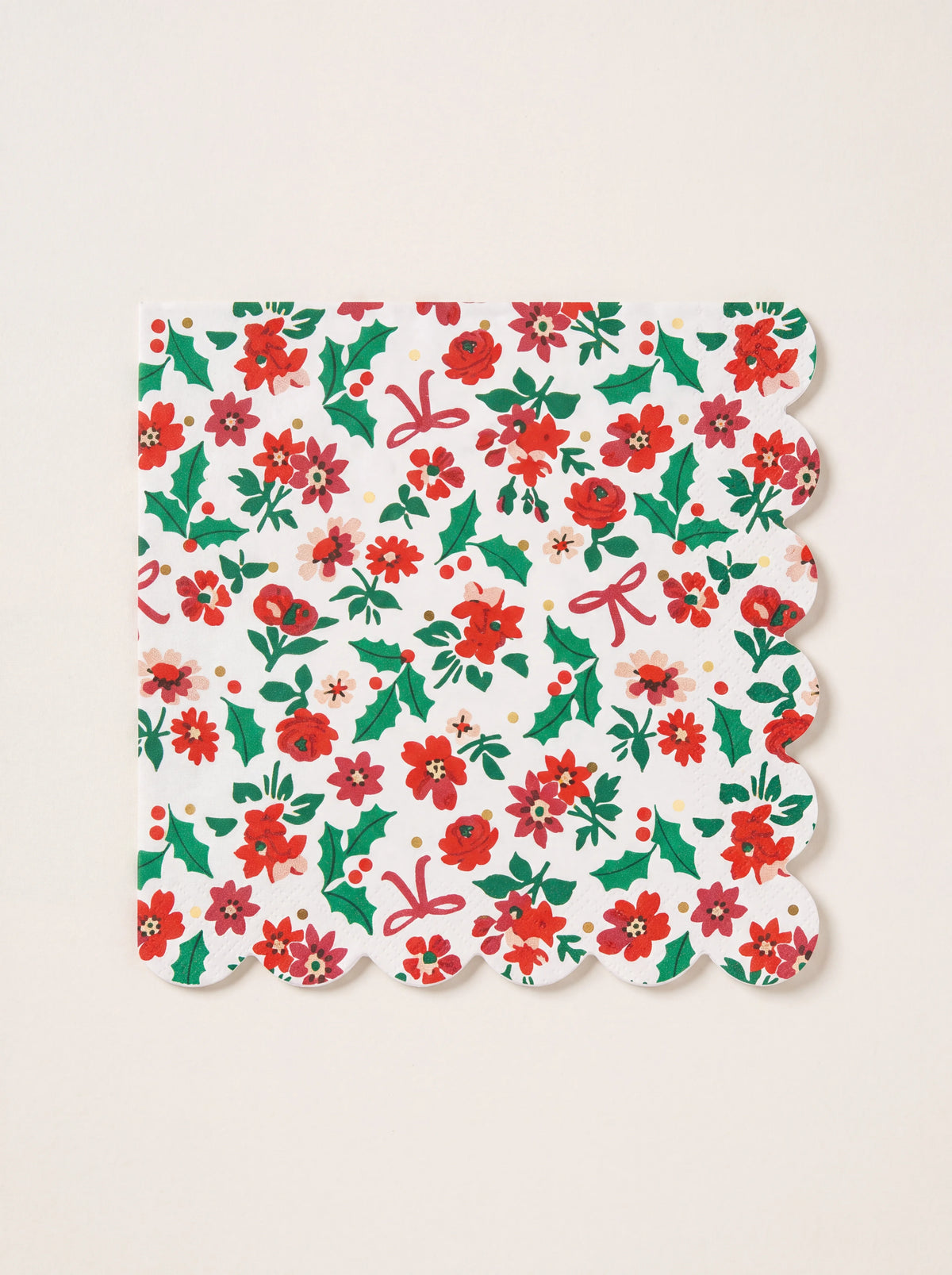 Square paper napkin with scalloped edges and a pattern of red flowers, green holly, bows and gold foil dots