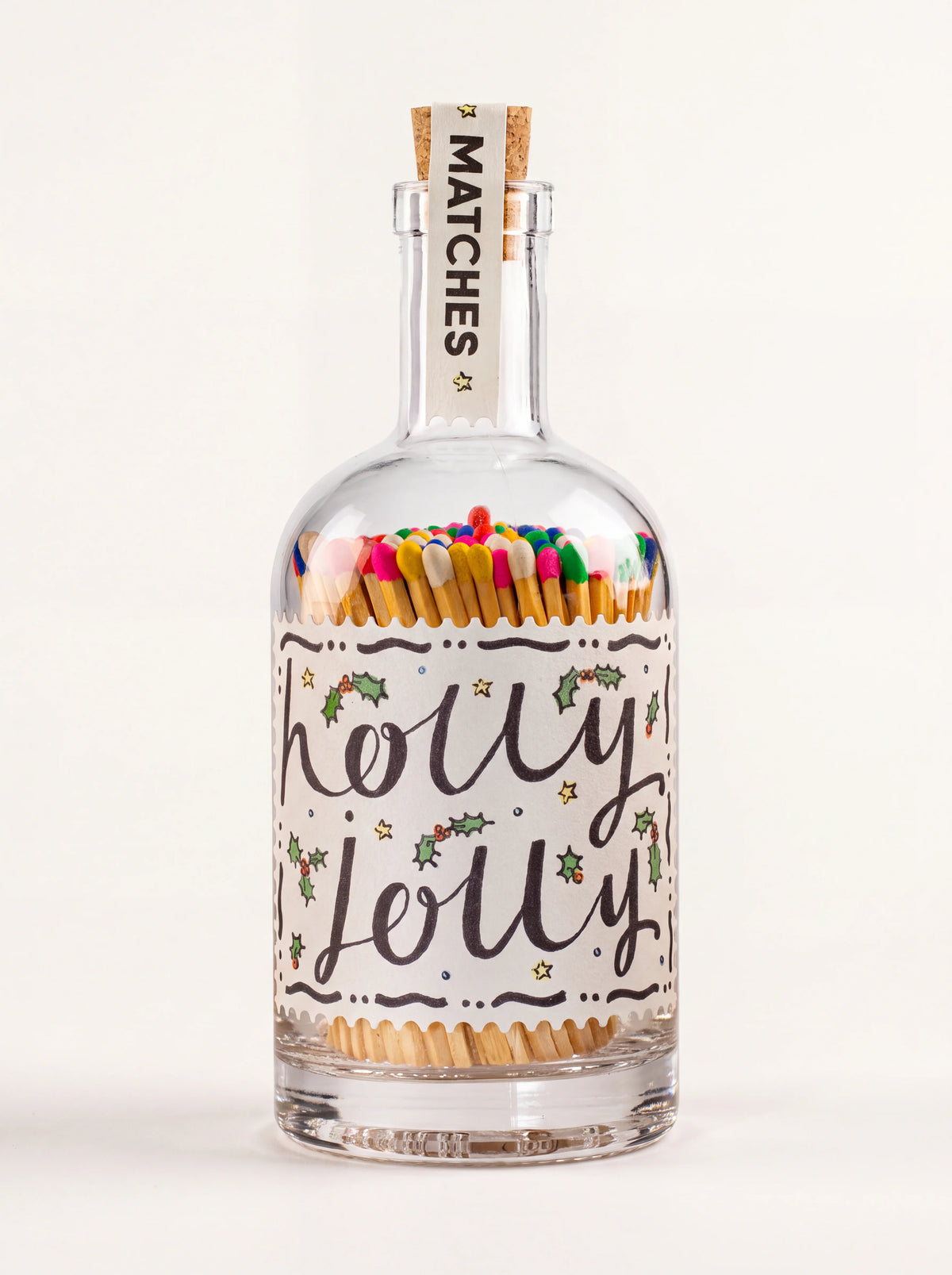 Clear glass bottle of multicoloured matches with a cork stopper and label reading Holly Jolly