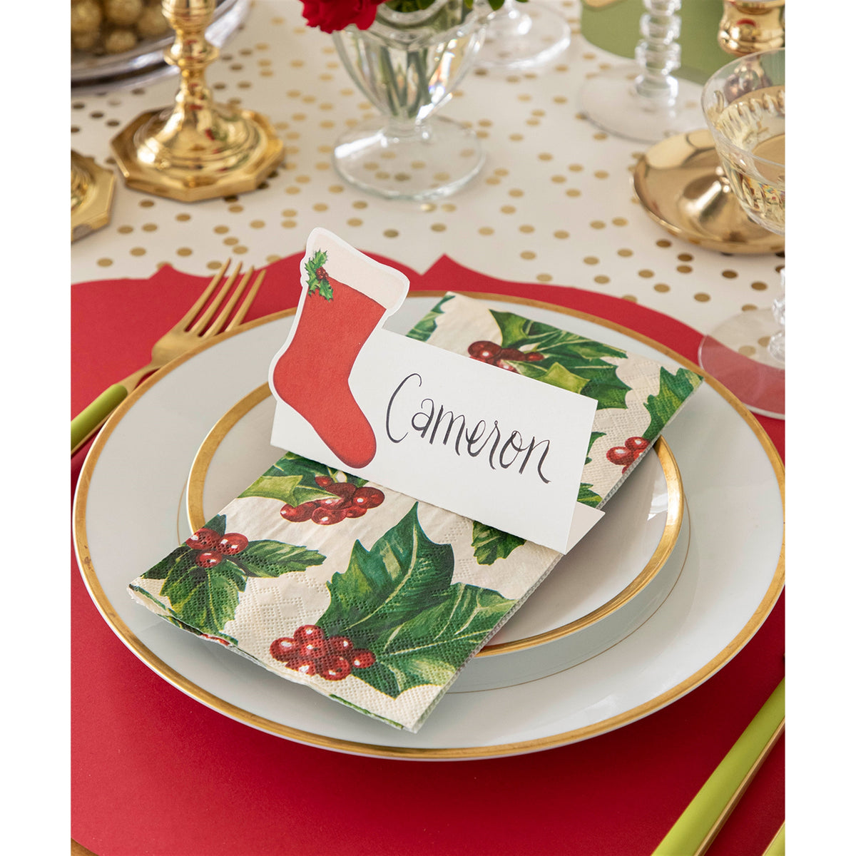 Holly paper guest napkin arranged on a plate with a stocking-shaped place card reading Cameron