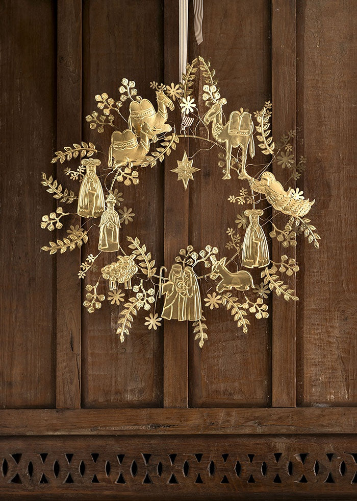 Golden nativity wreath hanging from a striped ribbon on a rustic dark wooden door