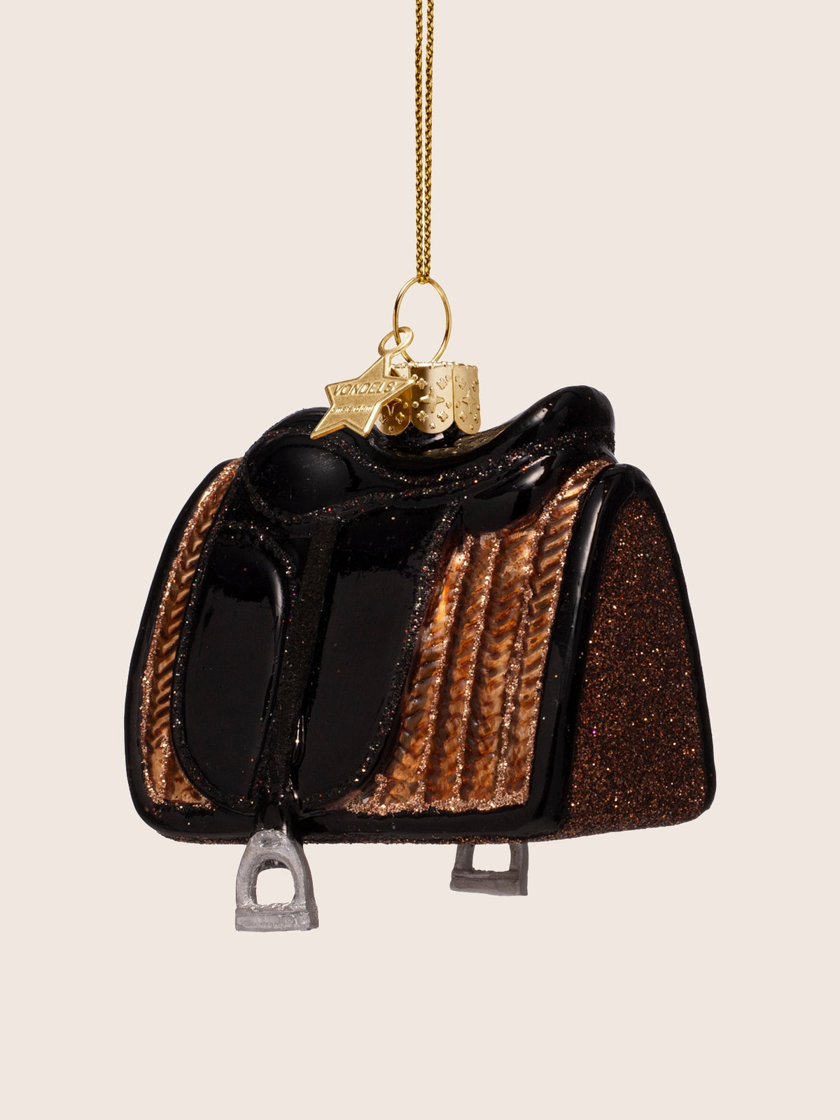 Three-quarter view of the glass saddle ornament, showing its curved shape, glitter trim and both stirrups below