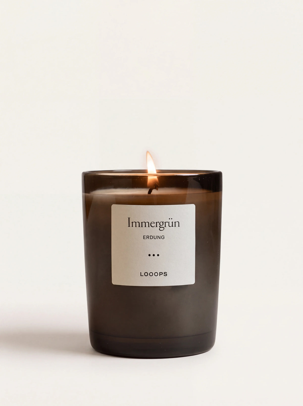 Lit scented candle in a dark glass jar with a white label reading Immergrün ERDUNG LOOOPS