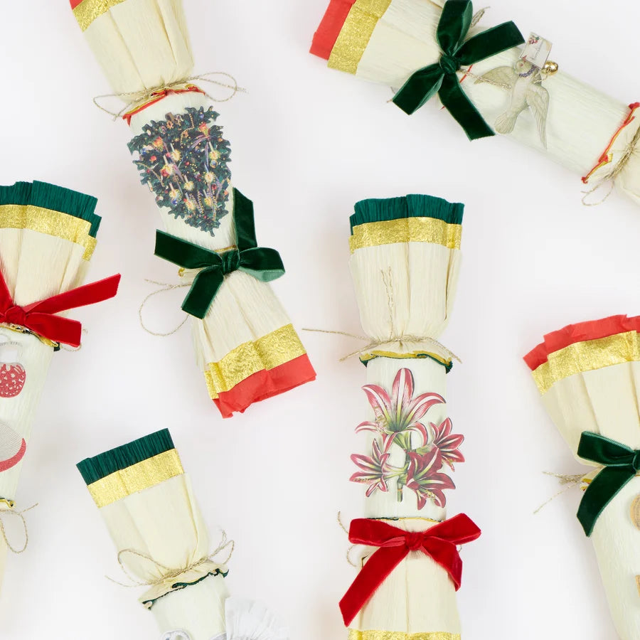 Crepe-paper Christmas crackers spread out, showing the illustrated motifs, metallic trim and velvet bows