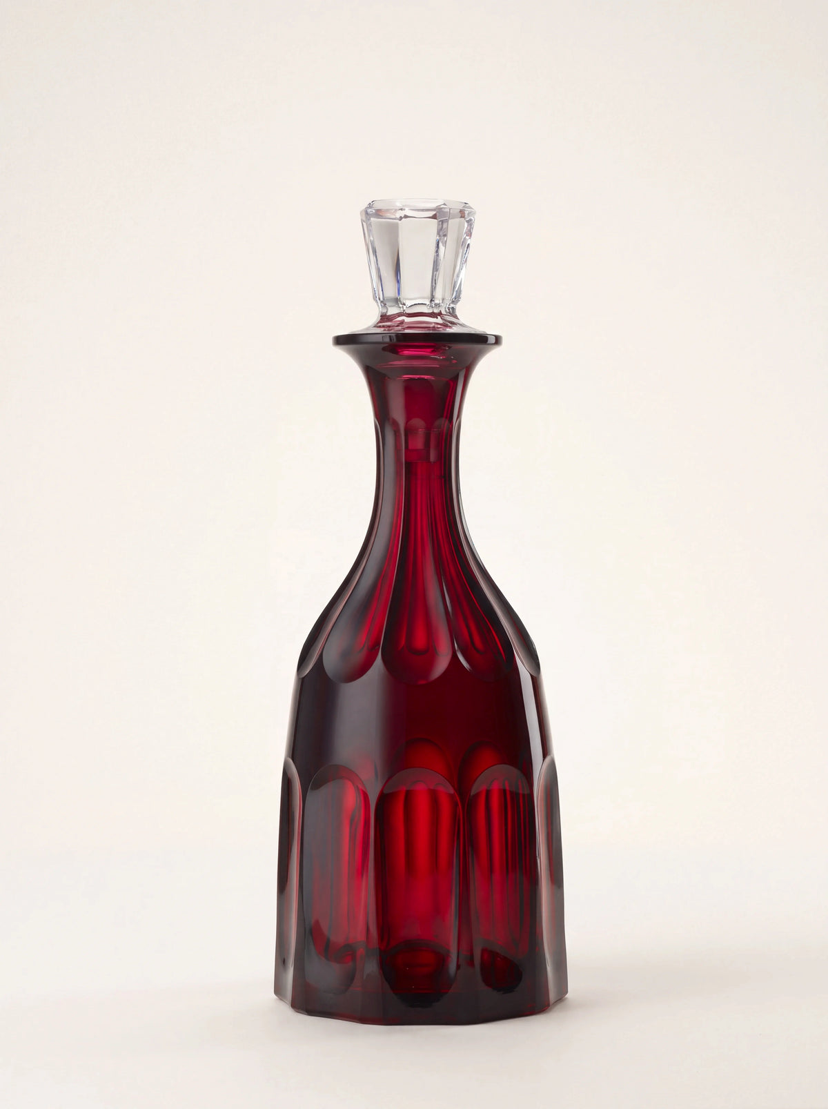 Ruby red acrylic bottle with arched facets, a tapered neck and a faceted clear stopper