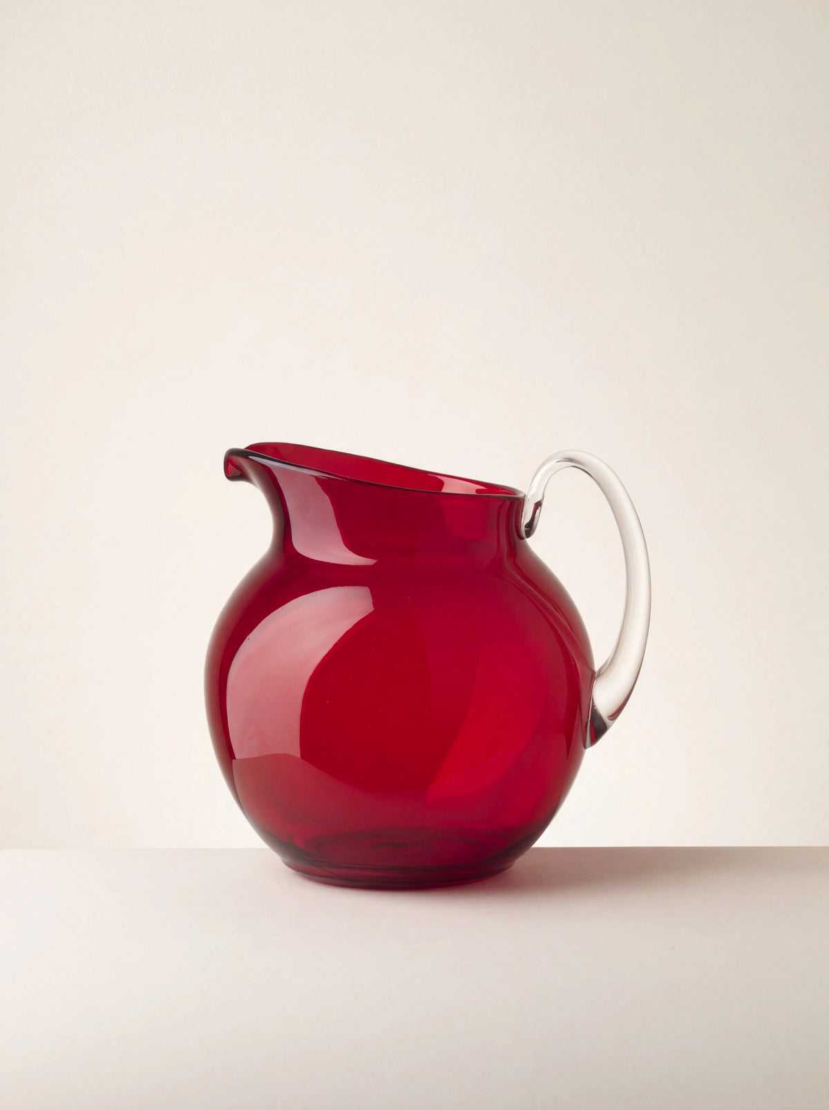 Round red acrylic pitcher with a pouring spout and clear curved handle