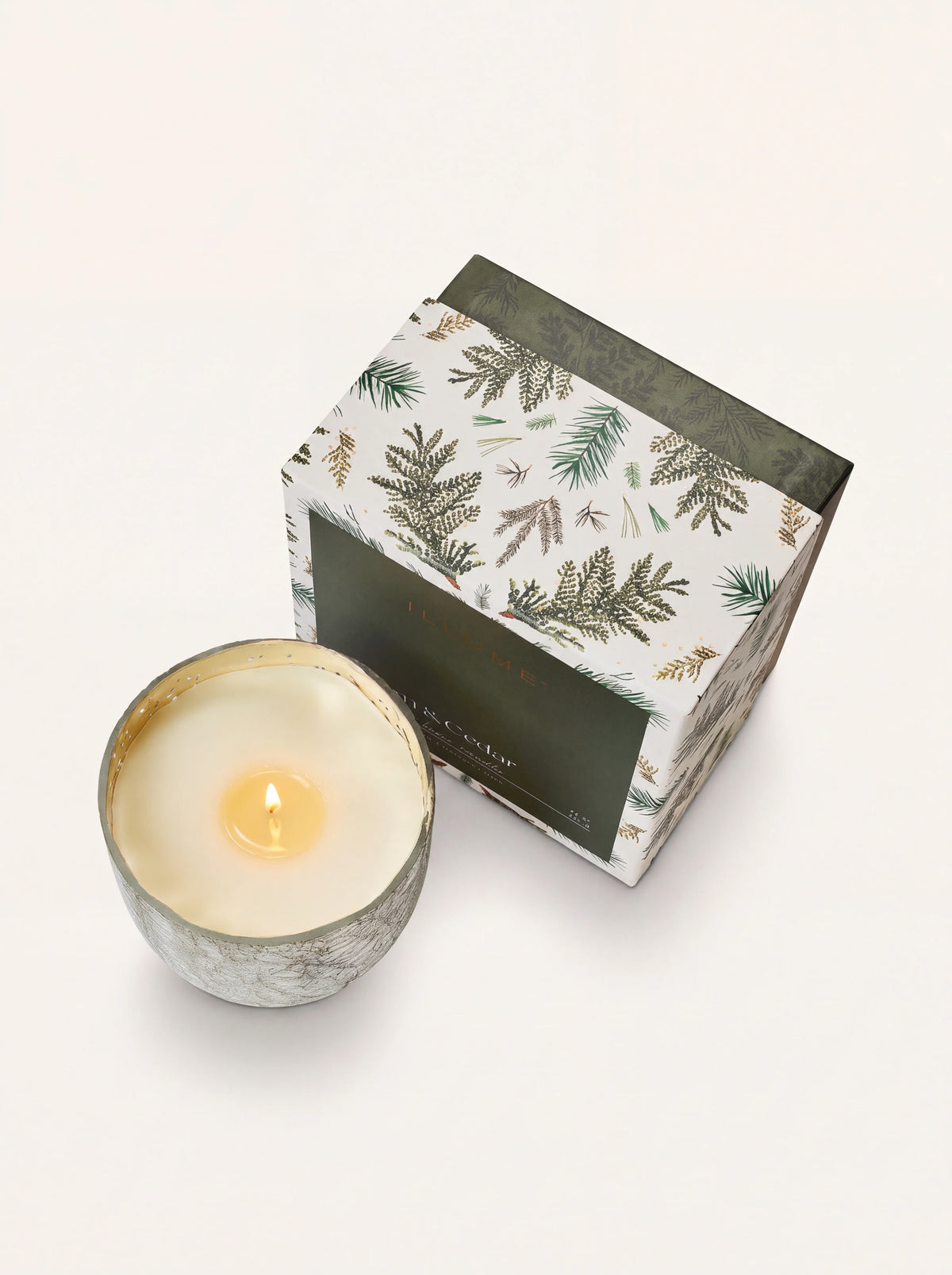 Lit scented candle with a burning wick and wax pool, viewed from above next to the pine-patterned box