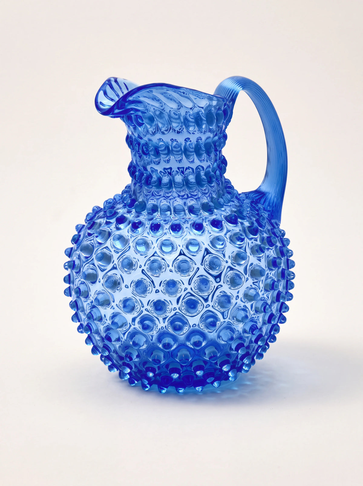 Blue glass jug with a raised hobnail pattern, bulbous shape, arched handle, and flared spout