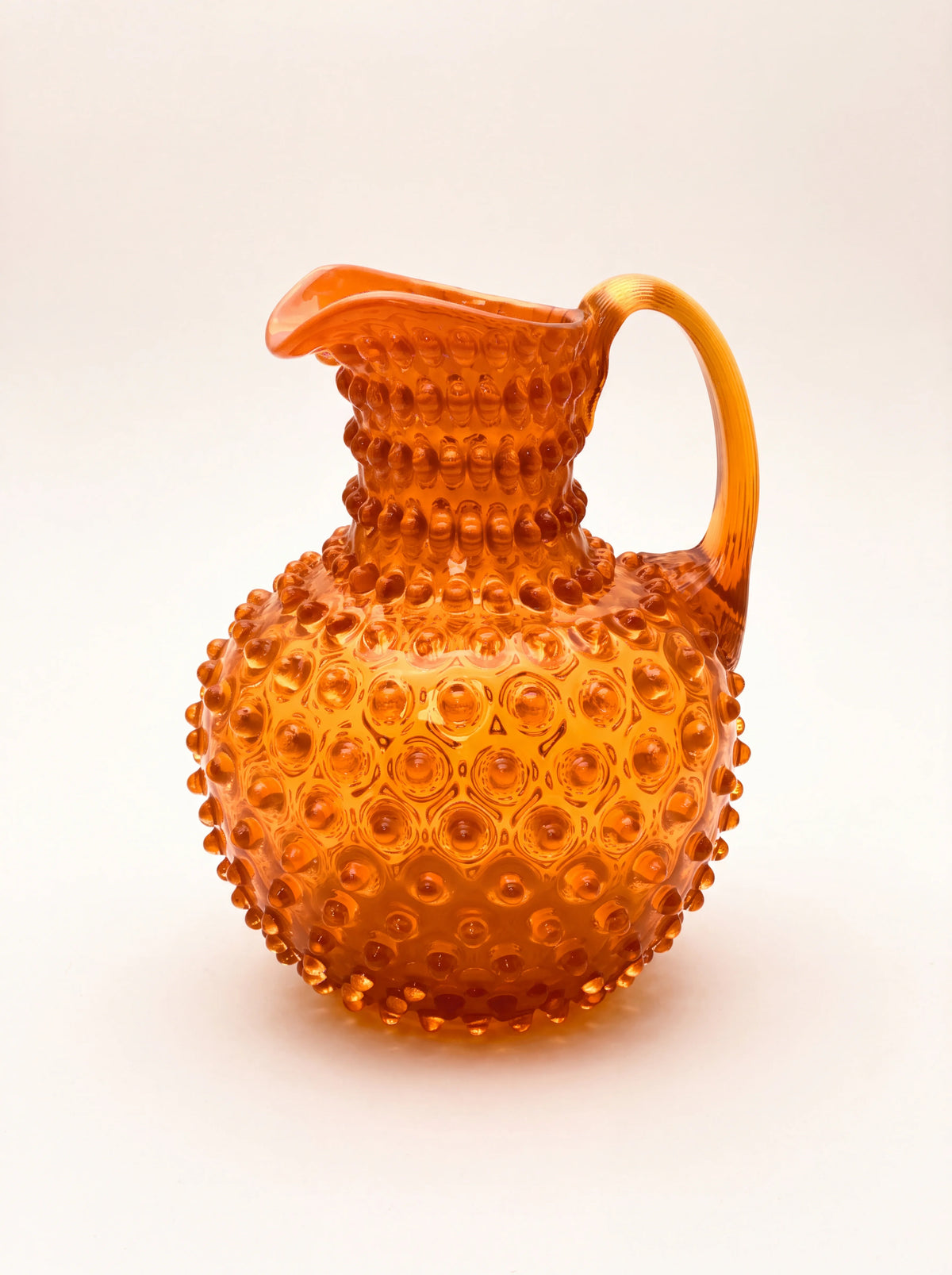 Orange hobnail glass jug with a bulbous body, curved pouring spout and arched handle