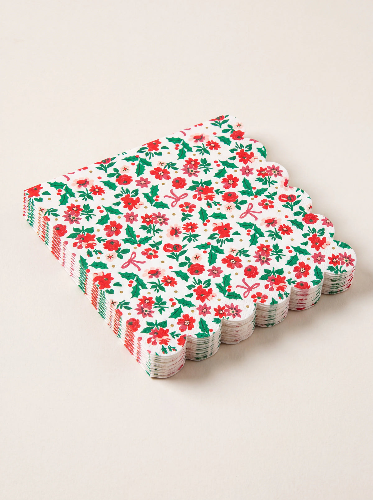Stack of white paper napkins with scalloped edges, red and pink floral holly pattern, and gold foil accents