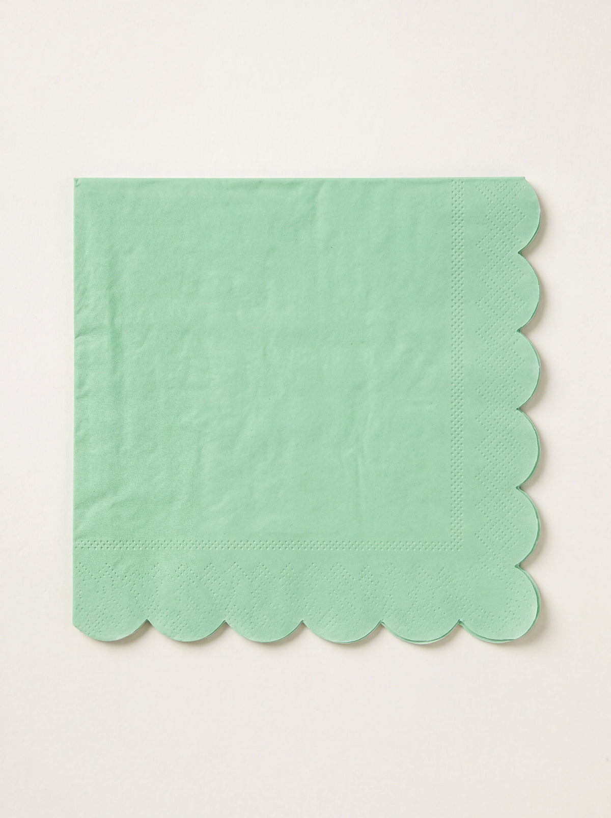 Square emerald green paper napkin folded with scalloped edges and an embossed border
