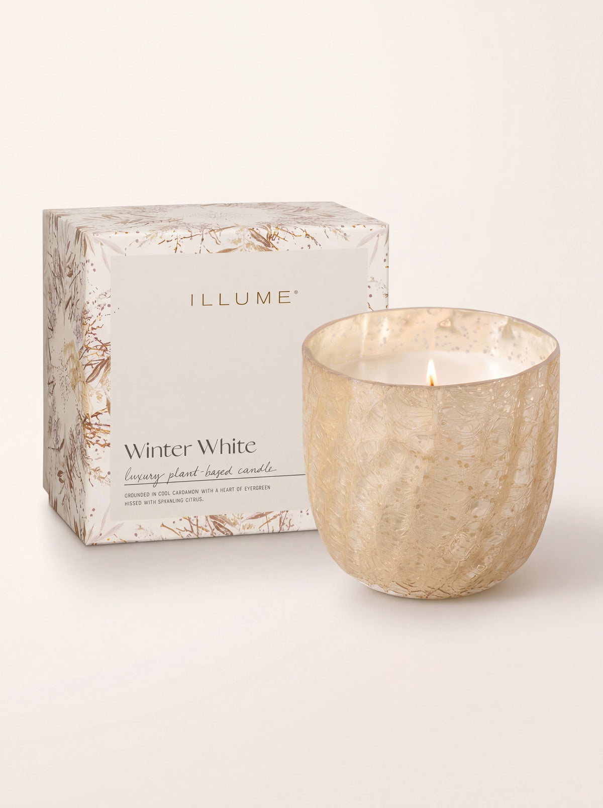 Lit candle beside its box reading 'ILLUME Winter White luxury plant-based candle