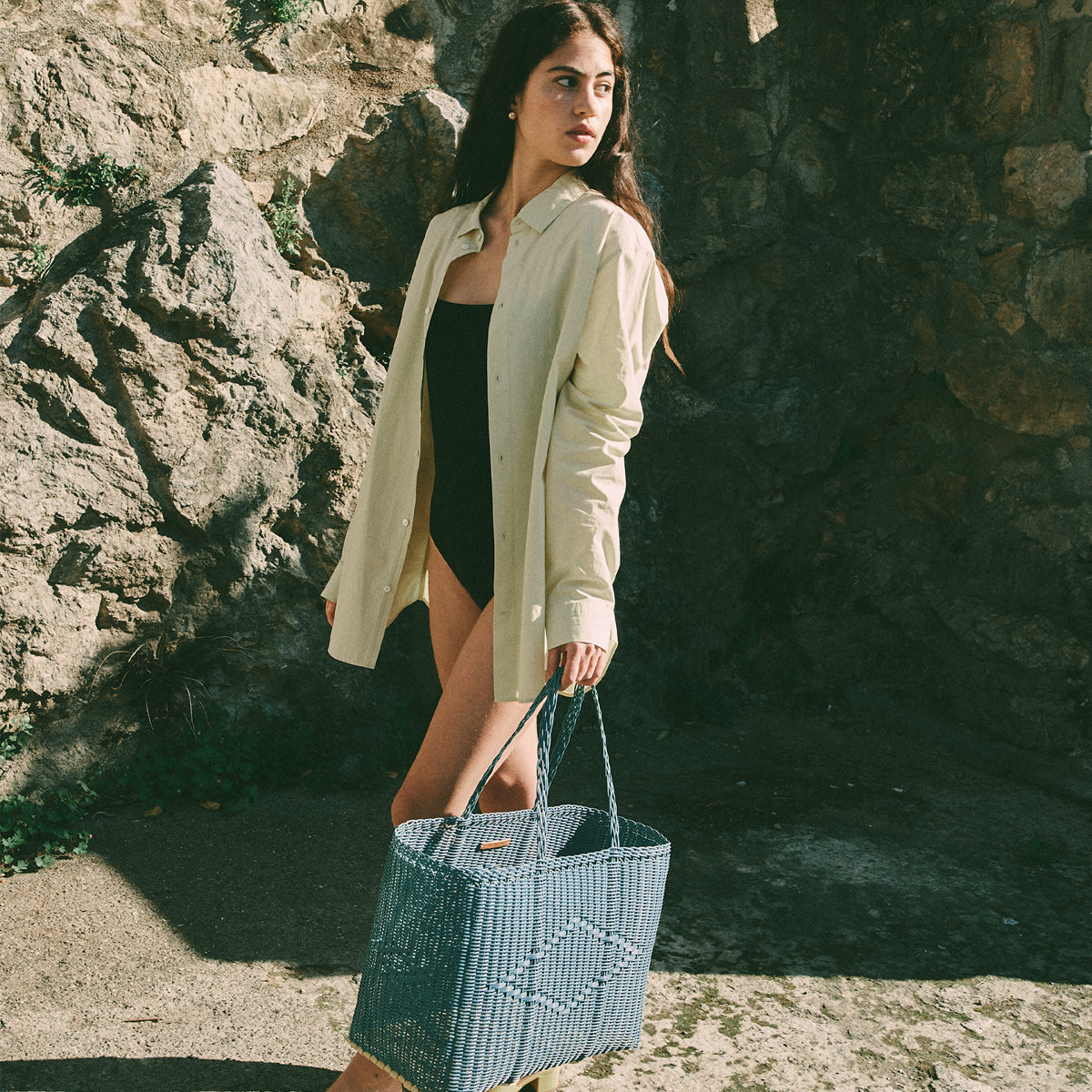 Woven plastic tote bag held in hand, showing its scale and open interior