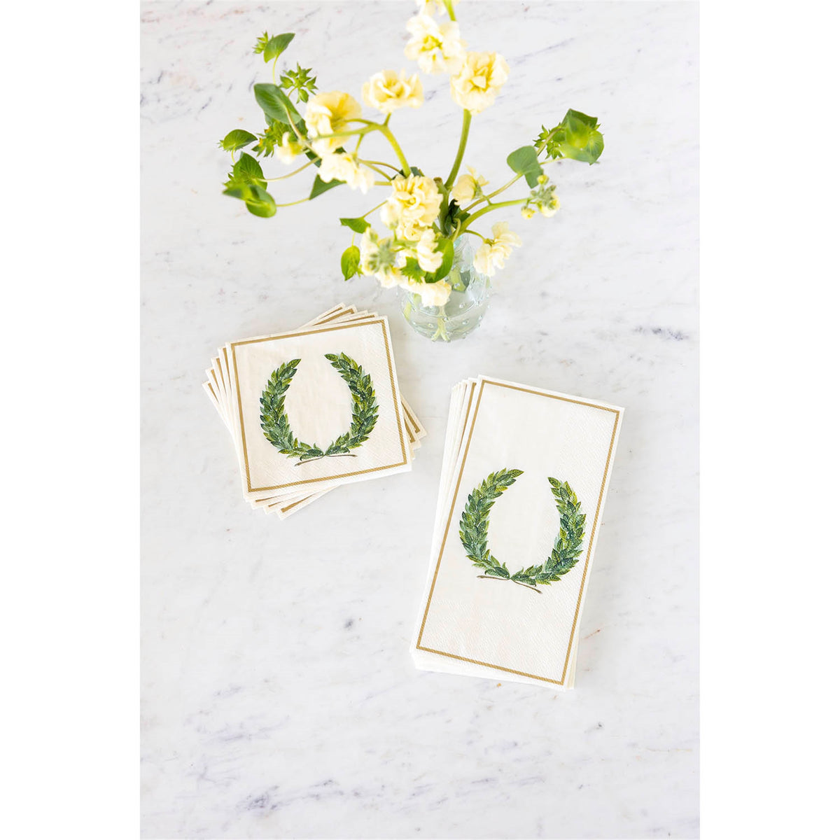 Folded paper guest napkins stacked alongside matching square napkins on a marble surface