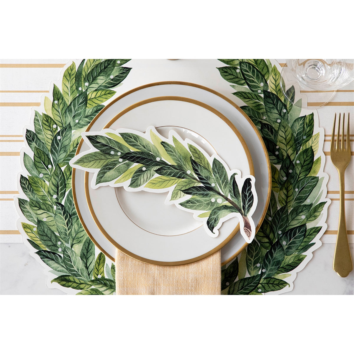 Laurel wreath paper placemat framing a gold-rimmed dinner plate in a table setting
