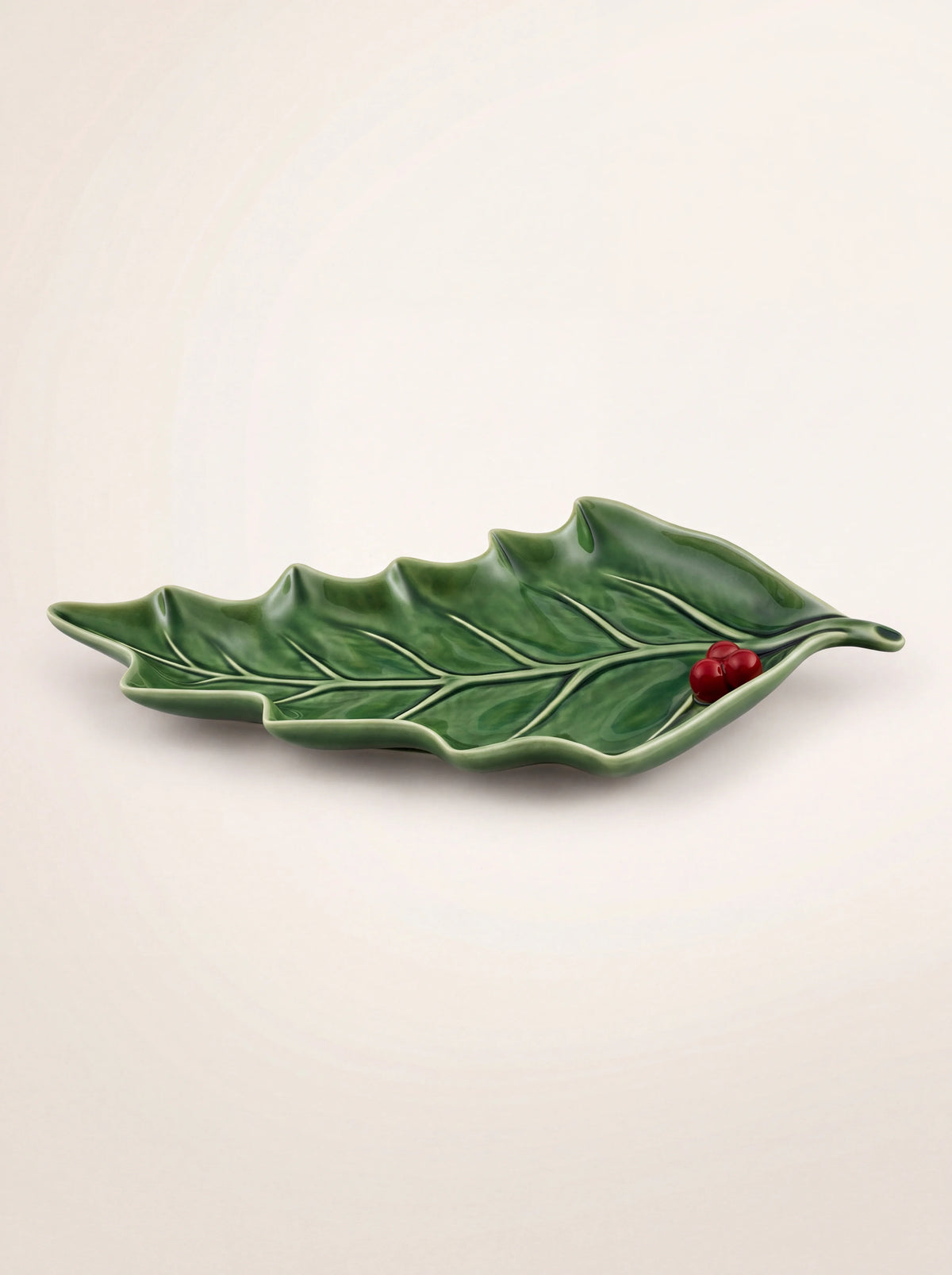 Green glazed earthenware dish shaped like a holly leaf with relief veins and red berries at the stem