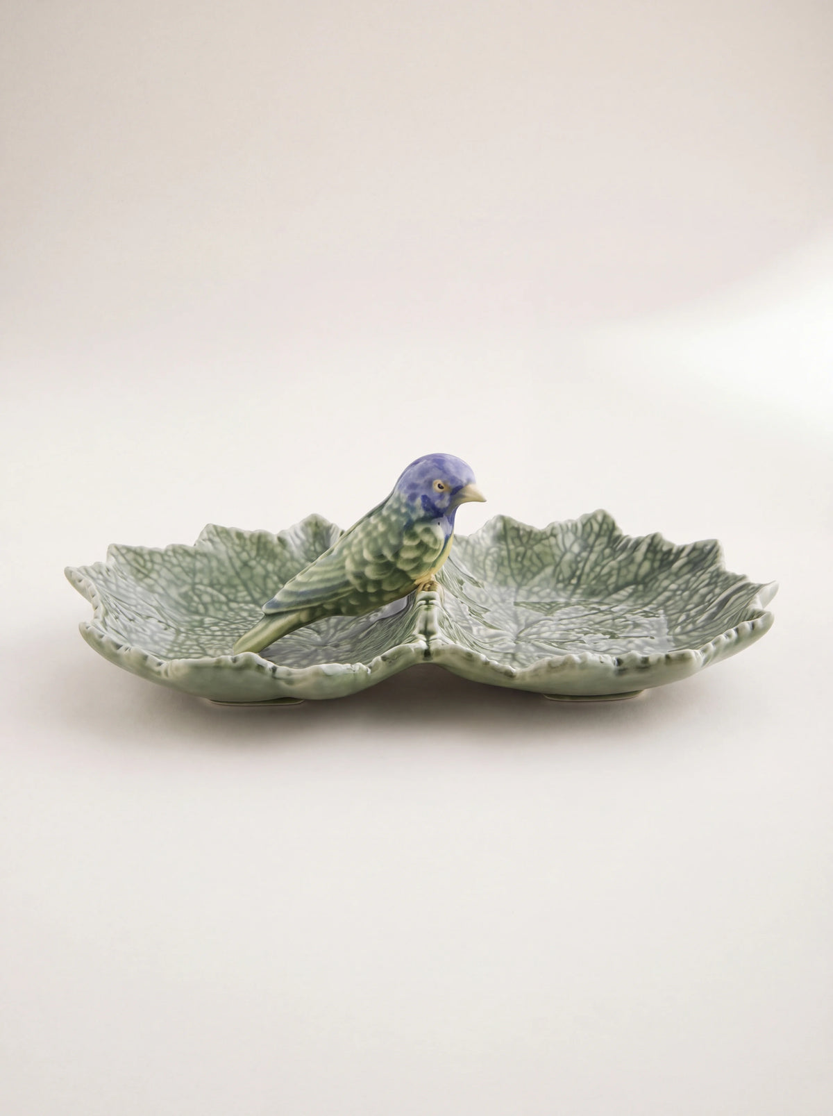 Green glazed earthenware dish shaped like two joined leaves with a blue bird perched in the centre