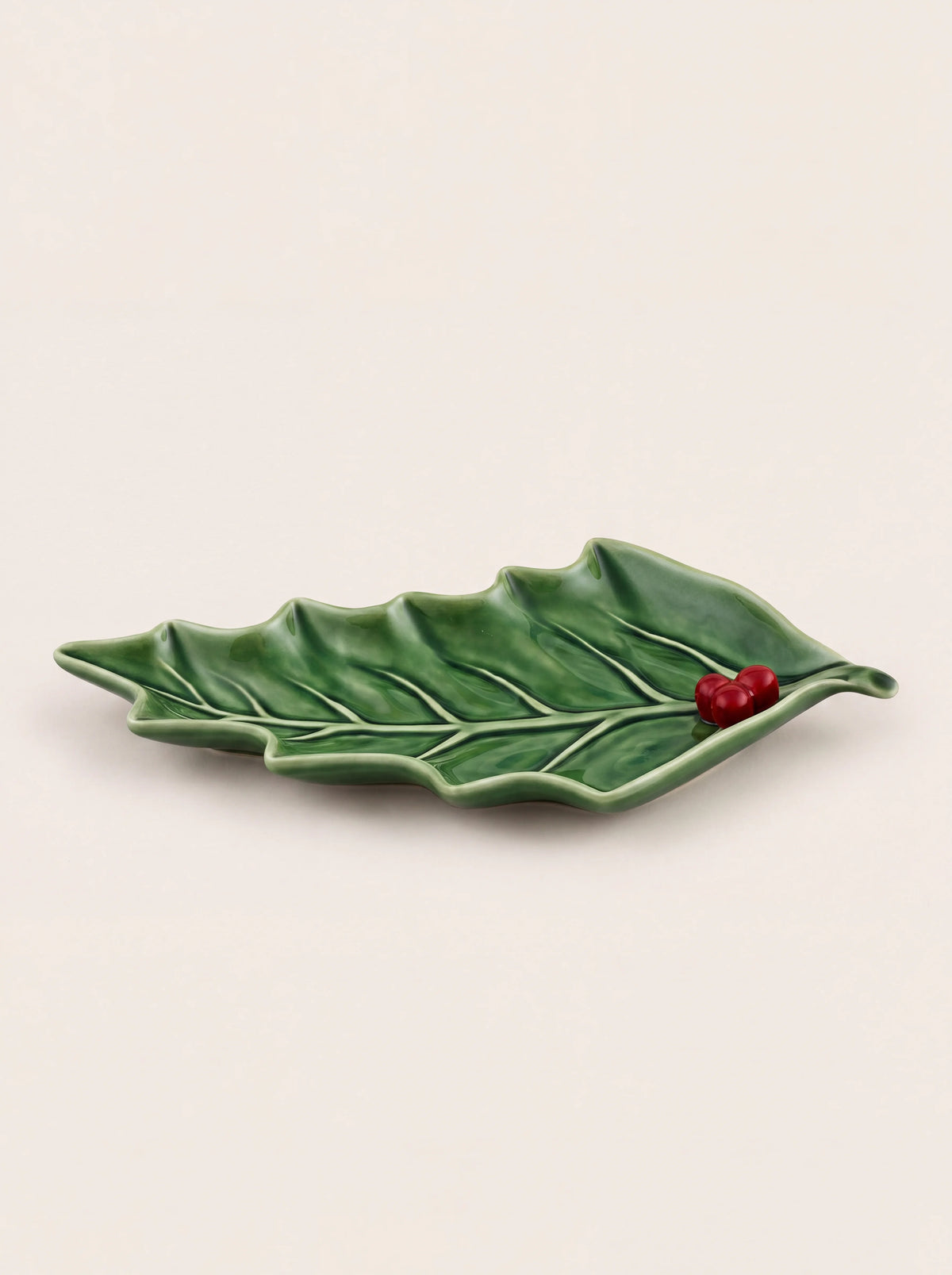 Glazed green earthenware dish shaped like a holly leaf with raised veins and three red berries at the stem