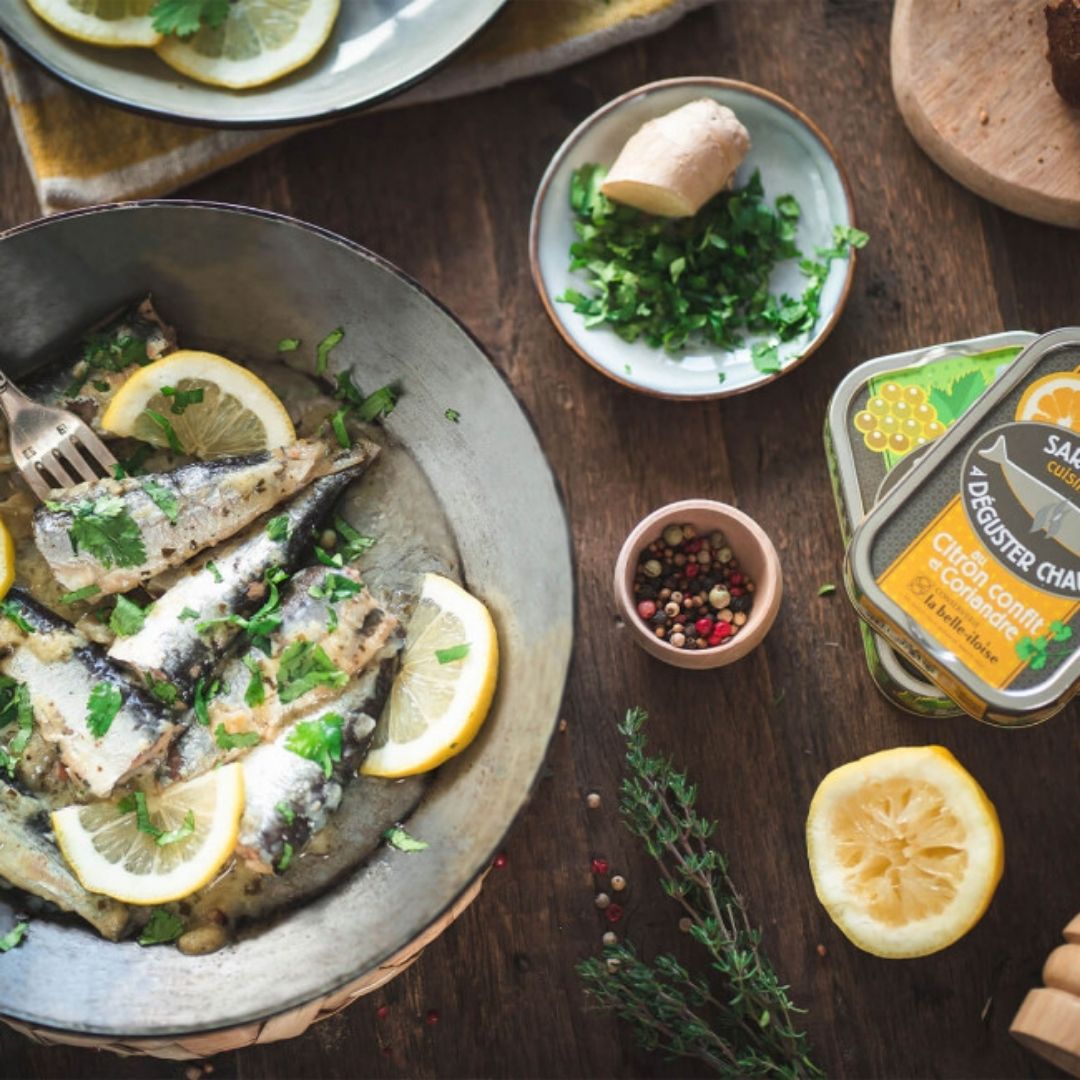 Warm sardines served with lemon wedges and fresh coriander in a rustic metal skillet