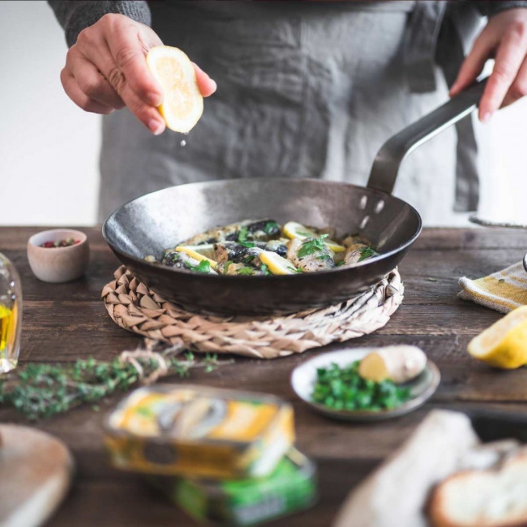 Fresh lemon being squeezed by hand over sardines heating in a frying pan