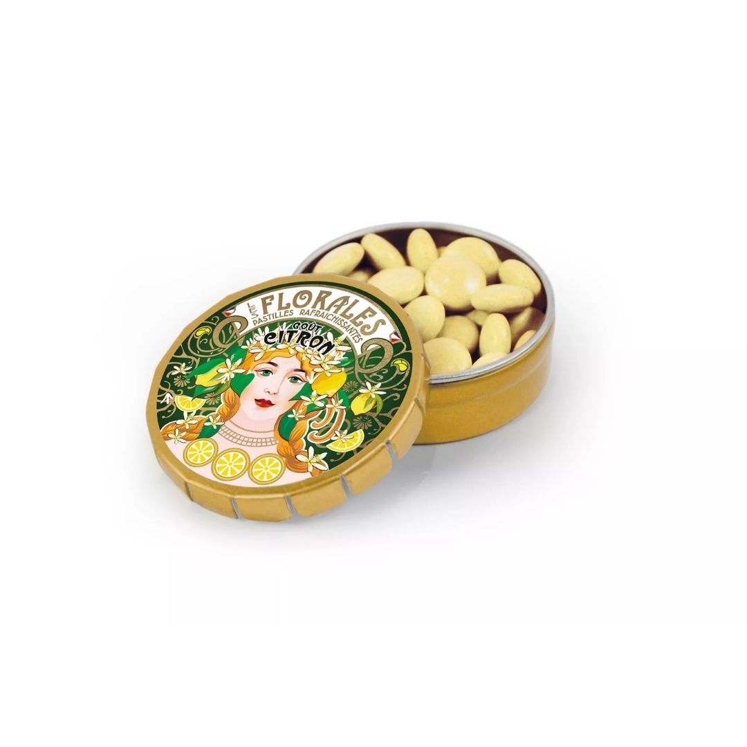 Open gold-coloured tin filled with pale yellow lemon pastilles, with the lid propped in front