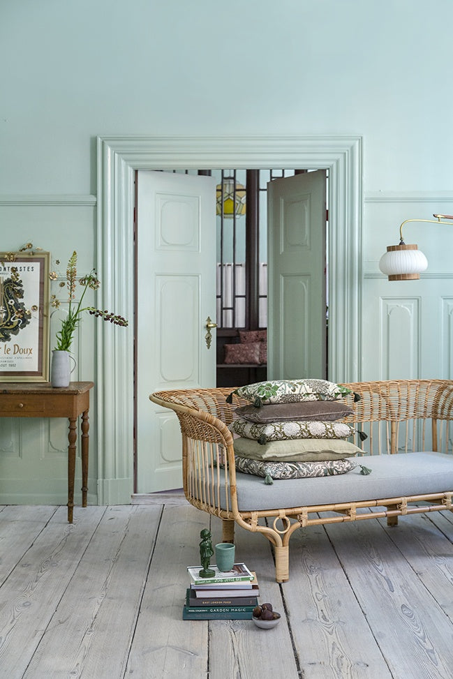 Celery green linen cushion stacked with other cushions on a rattan daybed