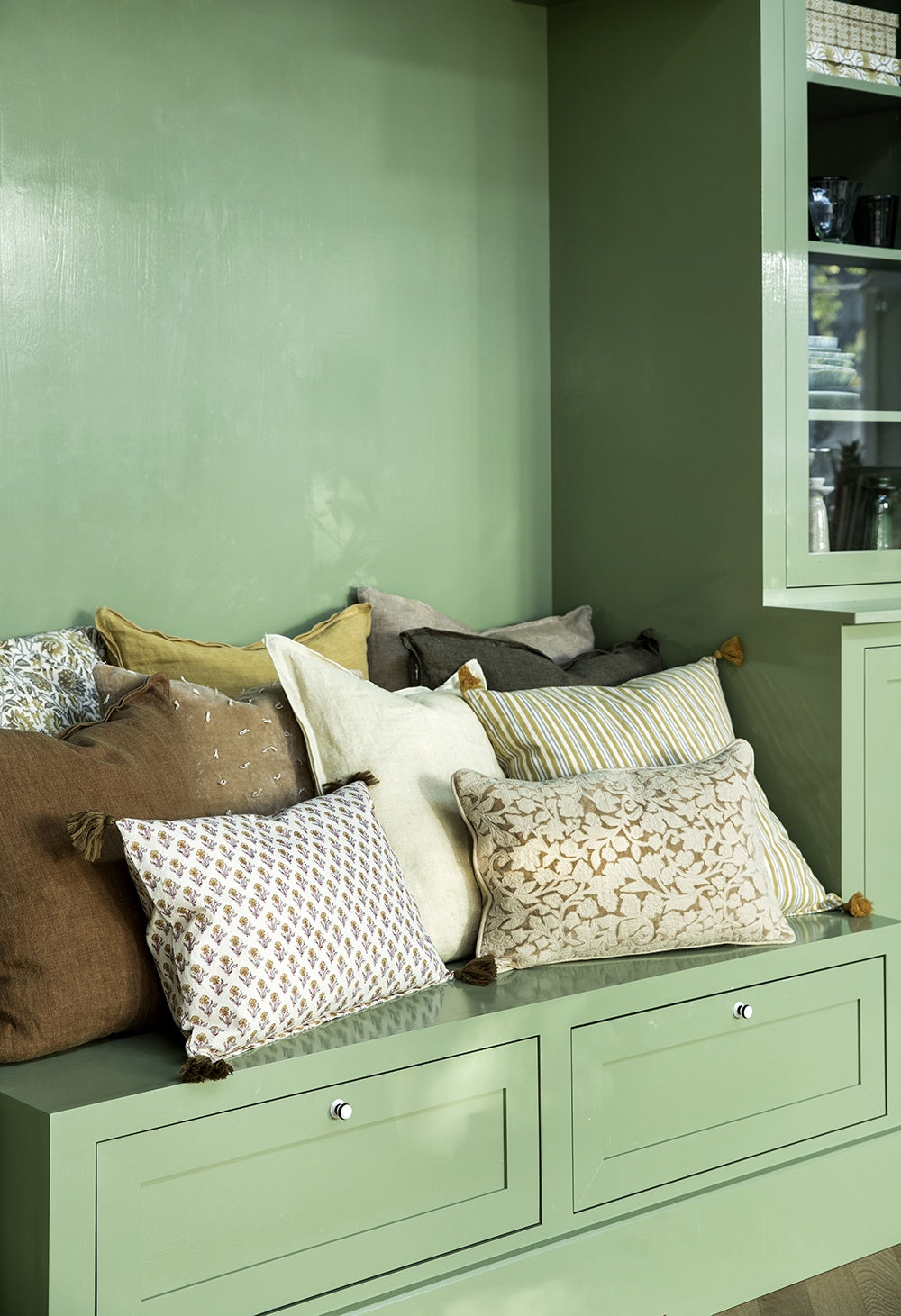 Linen cushion arranged among assorted cushions on a painted green bench