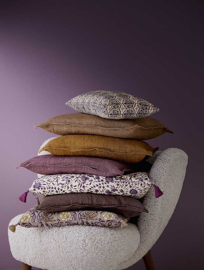 Fig linen cushion stacked among plain and patterned cushions on a textured armchair