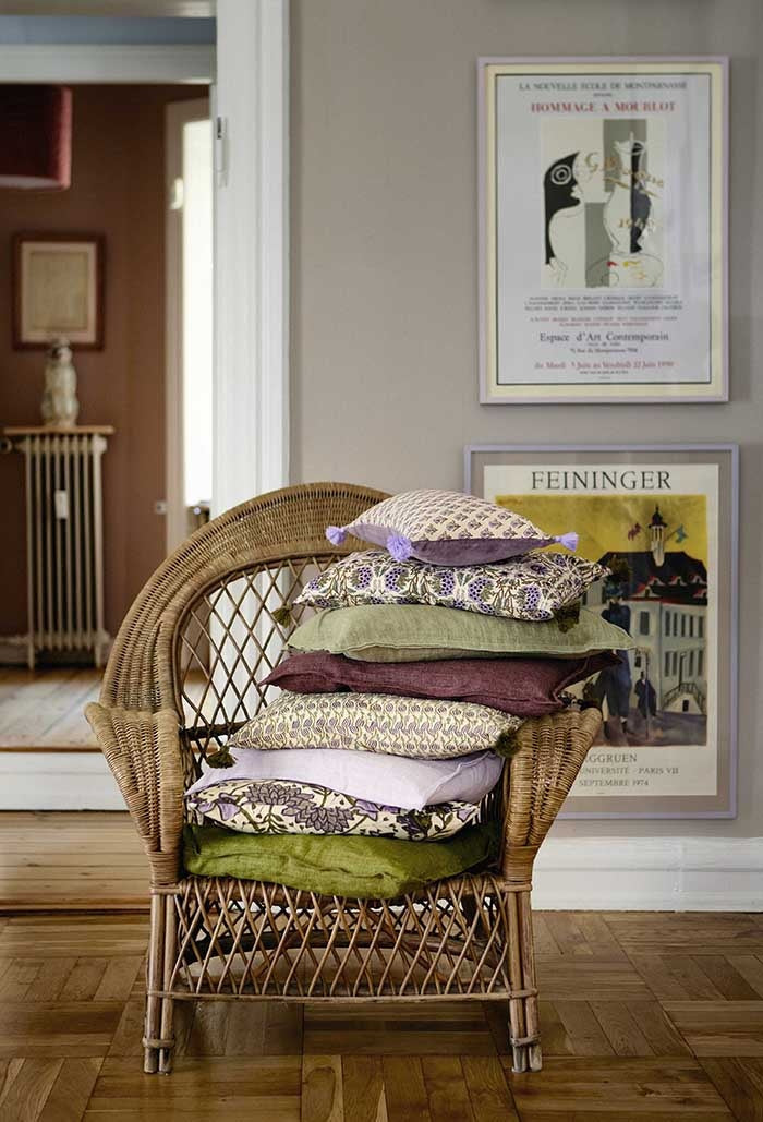 Fig linen cushion layered with floral and green cushions inside a wicker armchair