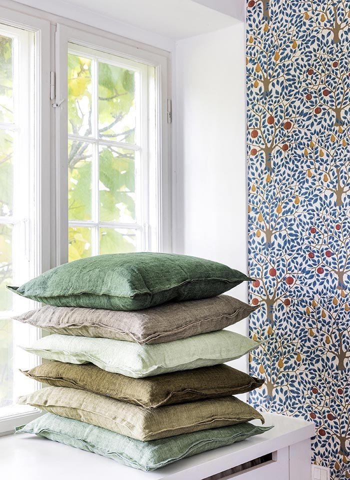 Stack of six linen cushions in various green and neutral shades beside a window