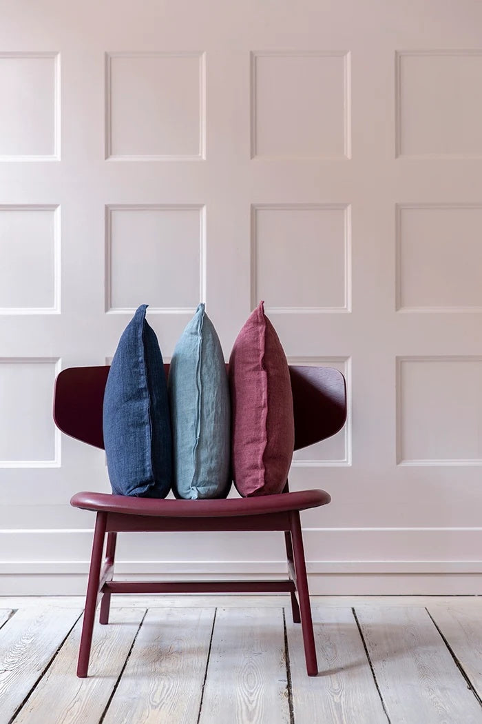 Tourmaline blue linen cushion standing upright from the side between navy and berry covers on a chair