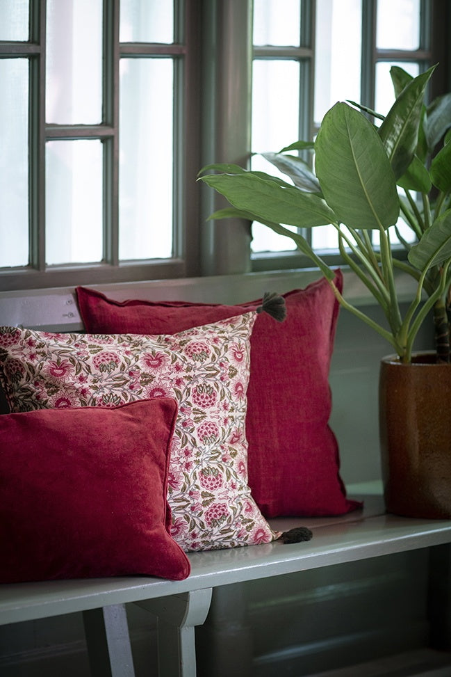 Wine-red linen cushion styled on a bench behind other cushions, next to a potted plant