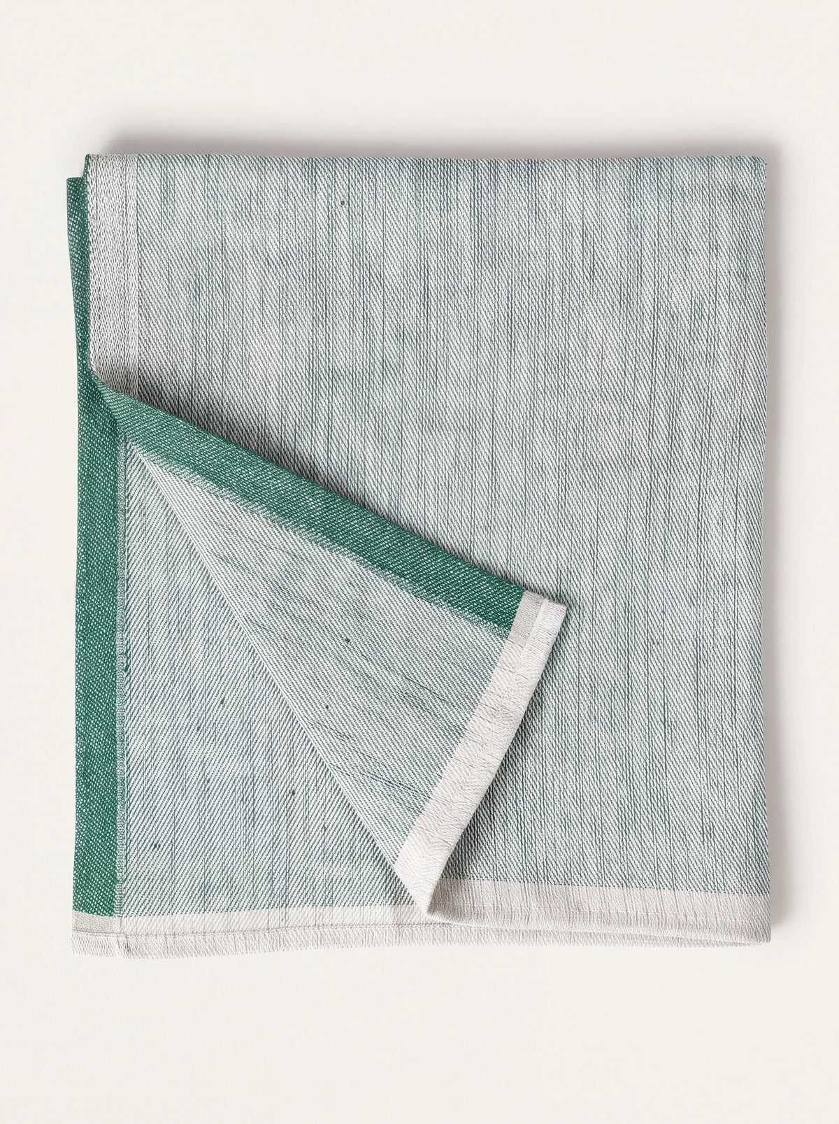 Pale green woven linen napkin with a dark green border, folded with a turned corner