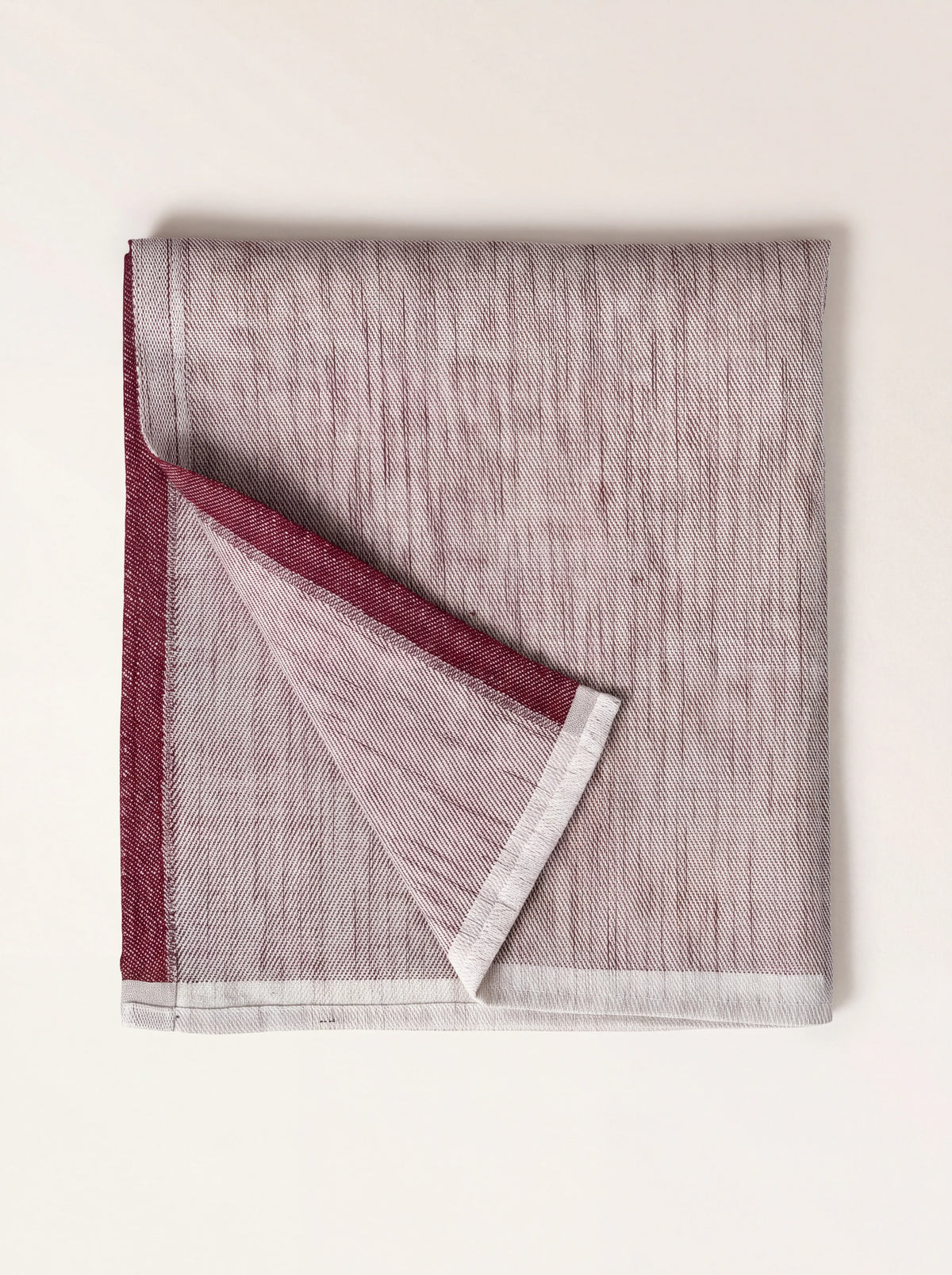 Bordeaux linen napkin folded with a turned-over corner, showing the two-tone weave and borders