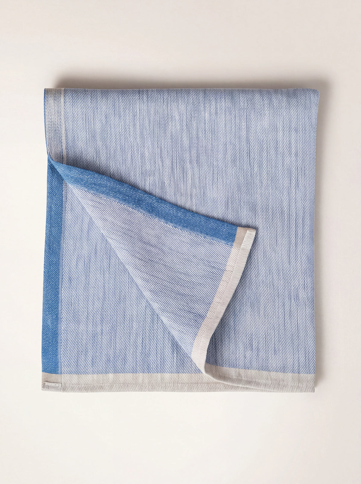 Folded blue linen napkin showing its two-tone weave and contrasting border stripes
