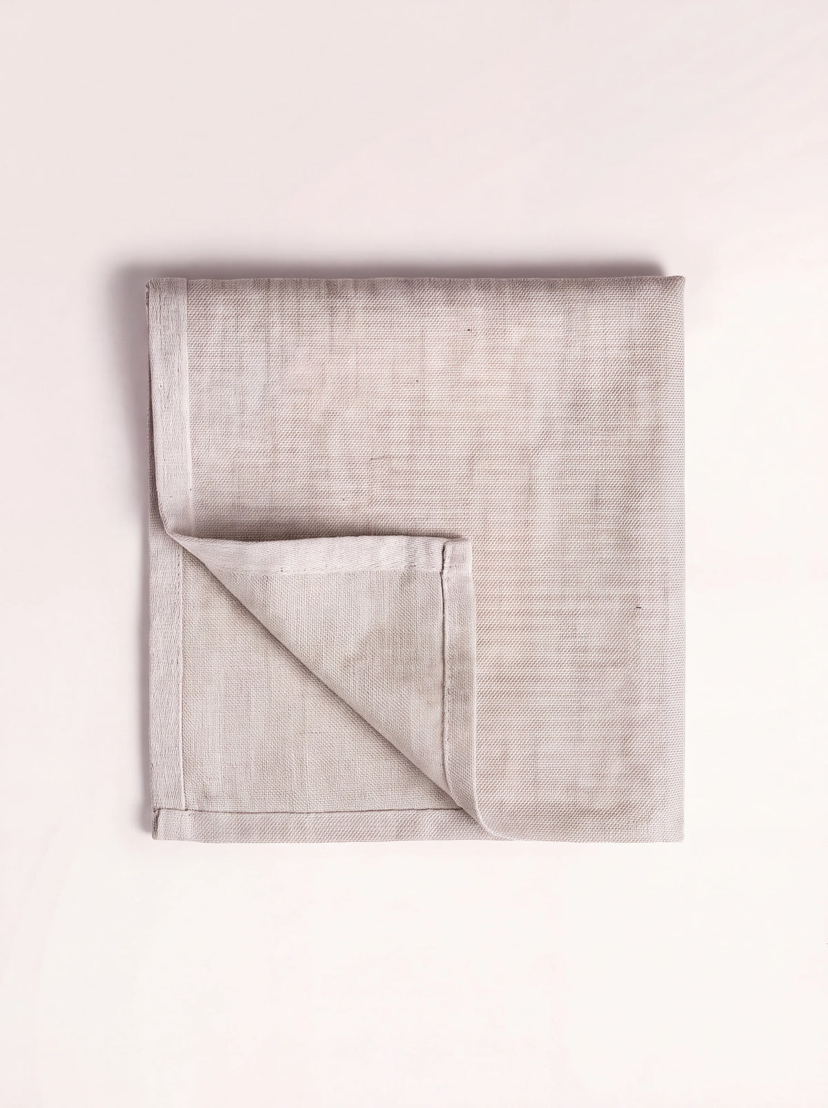 Square linen napkin in light beige, folded to show its stitched hem and woven texture