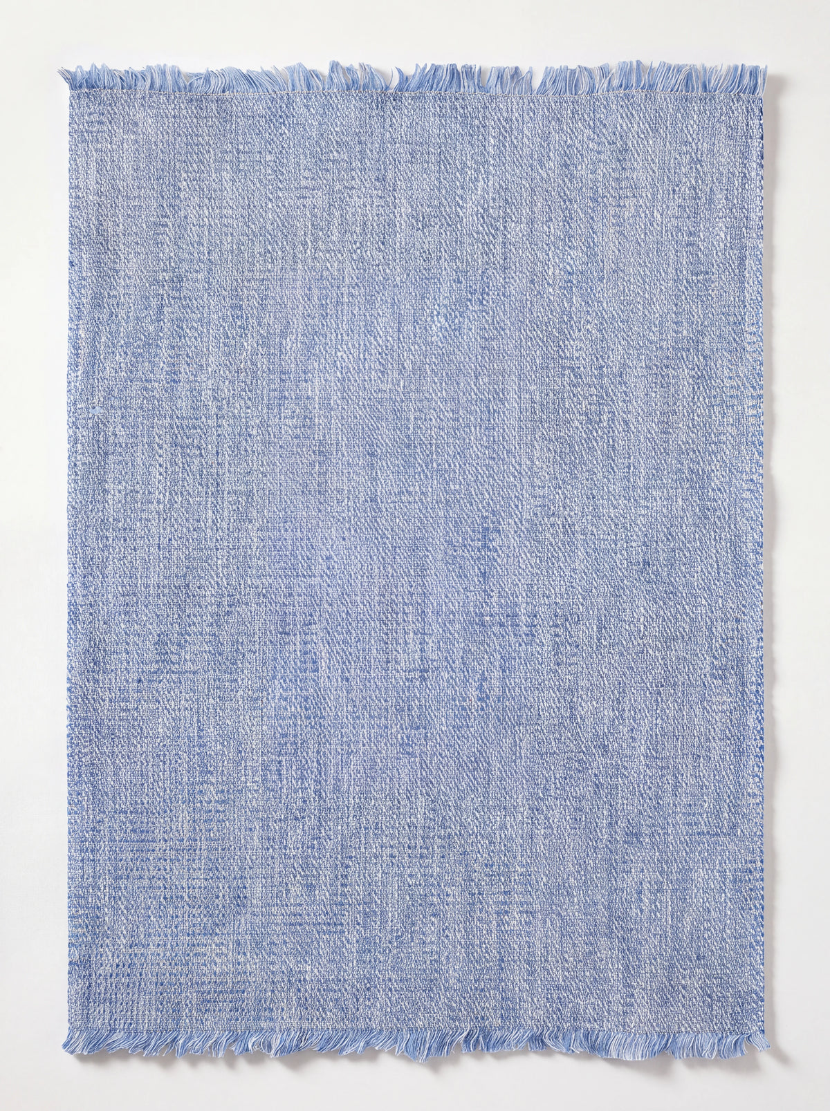 Rectangular blue washed linen placemat with fringed edges and a mélange weave