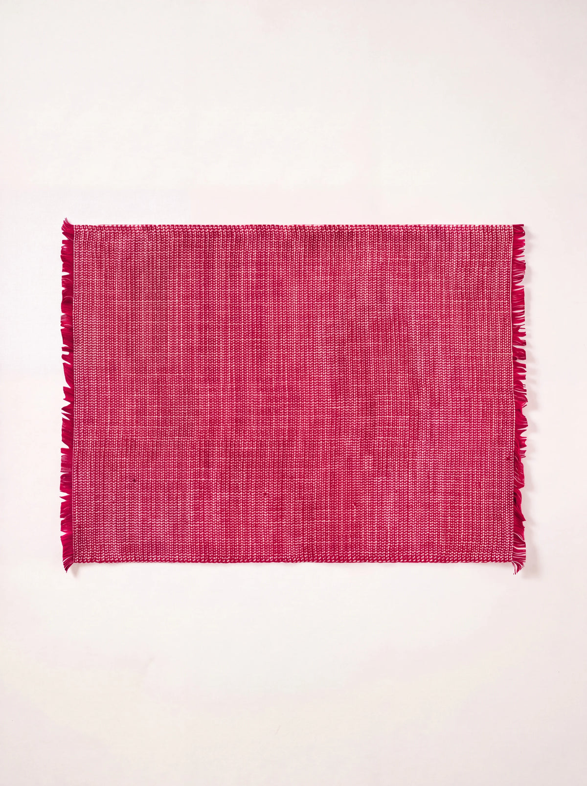 Rectangular red washed linen placemat with a woven texture and fringed edges