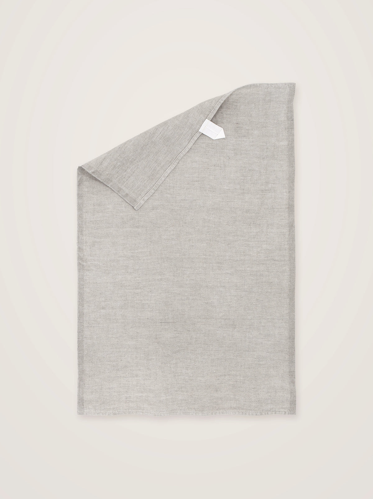 Washed linen tea towel in light grey, laid flat with one top corner turned down