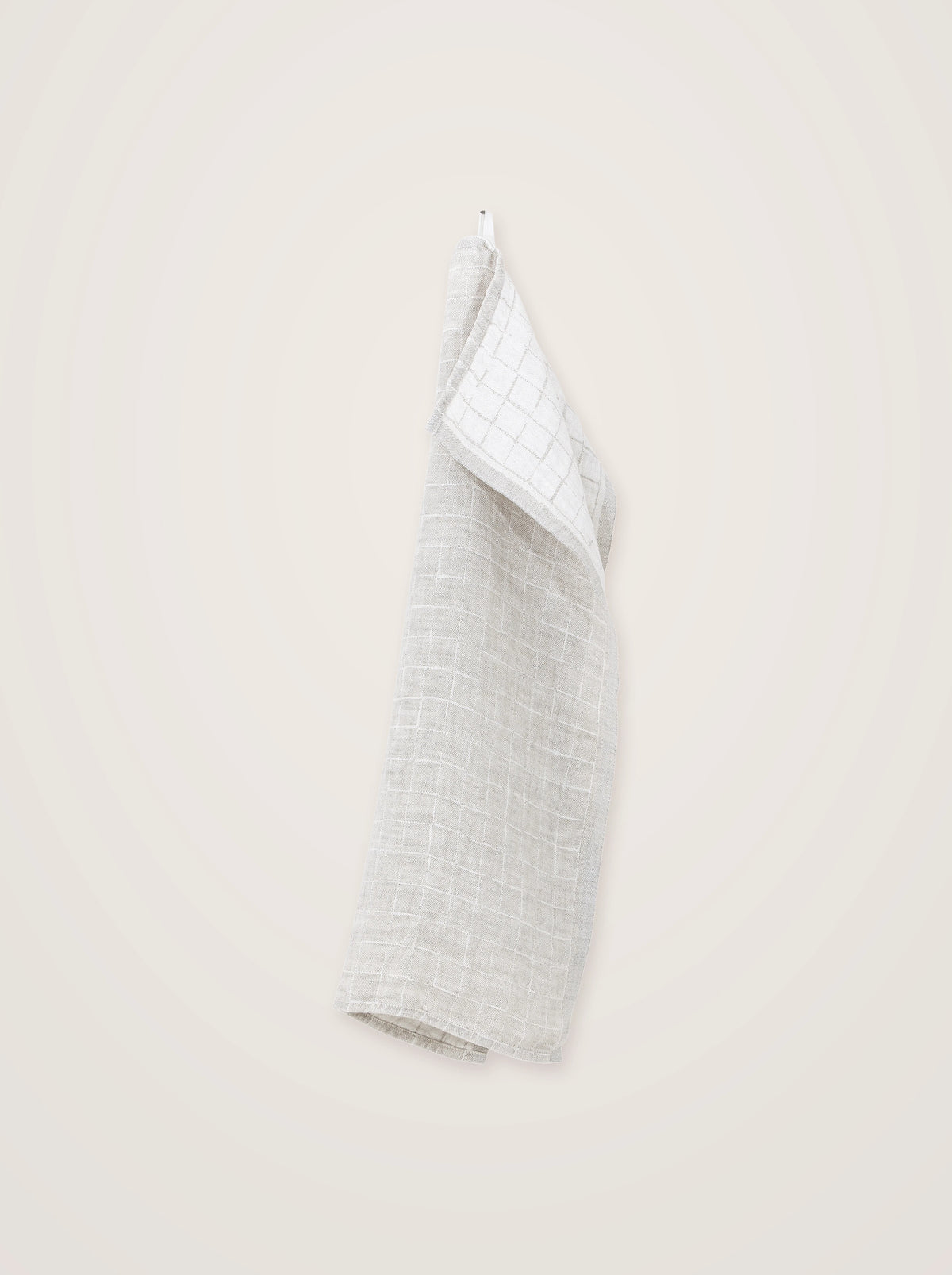 Beige washed linen towel hanging by a loop, showing its grid pattern and folded contrasting reverse