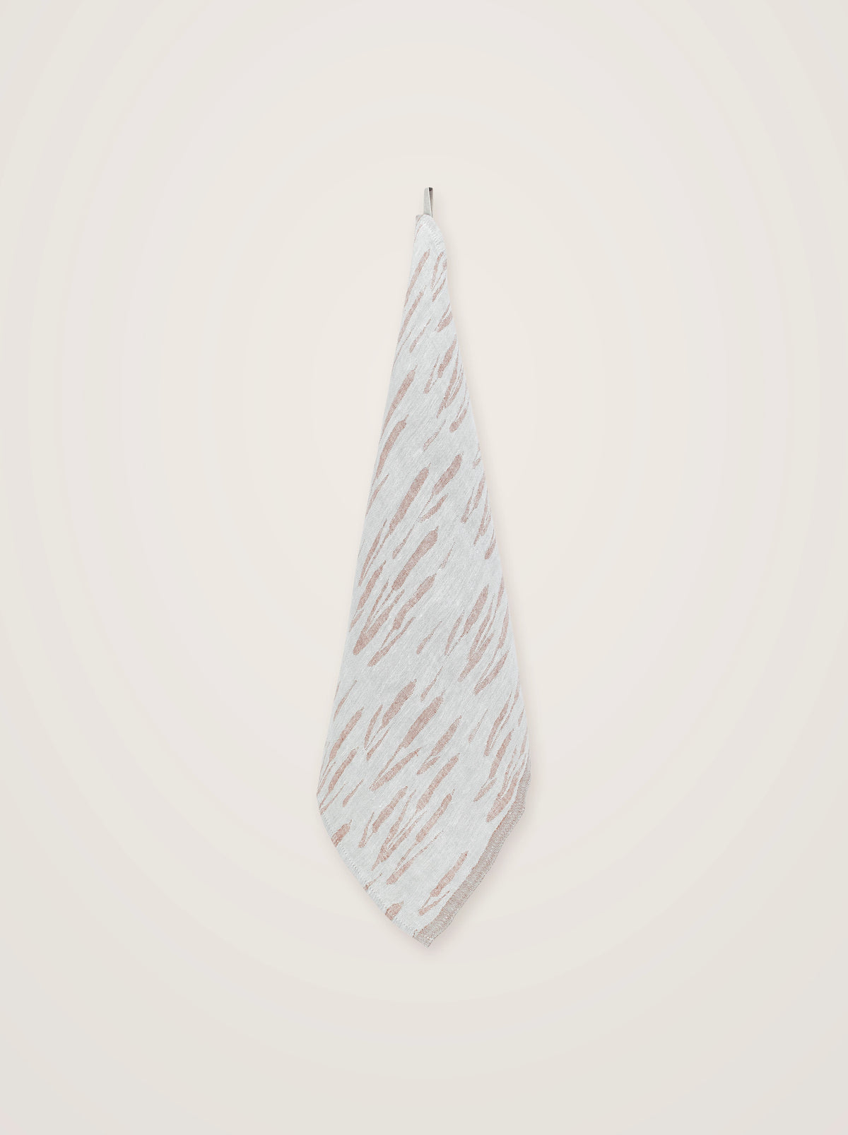 Washed linen towel hanging by its corner loop, showing the draped fabric and woven grey-cinnamon pattern