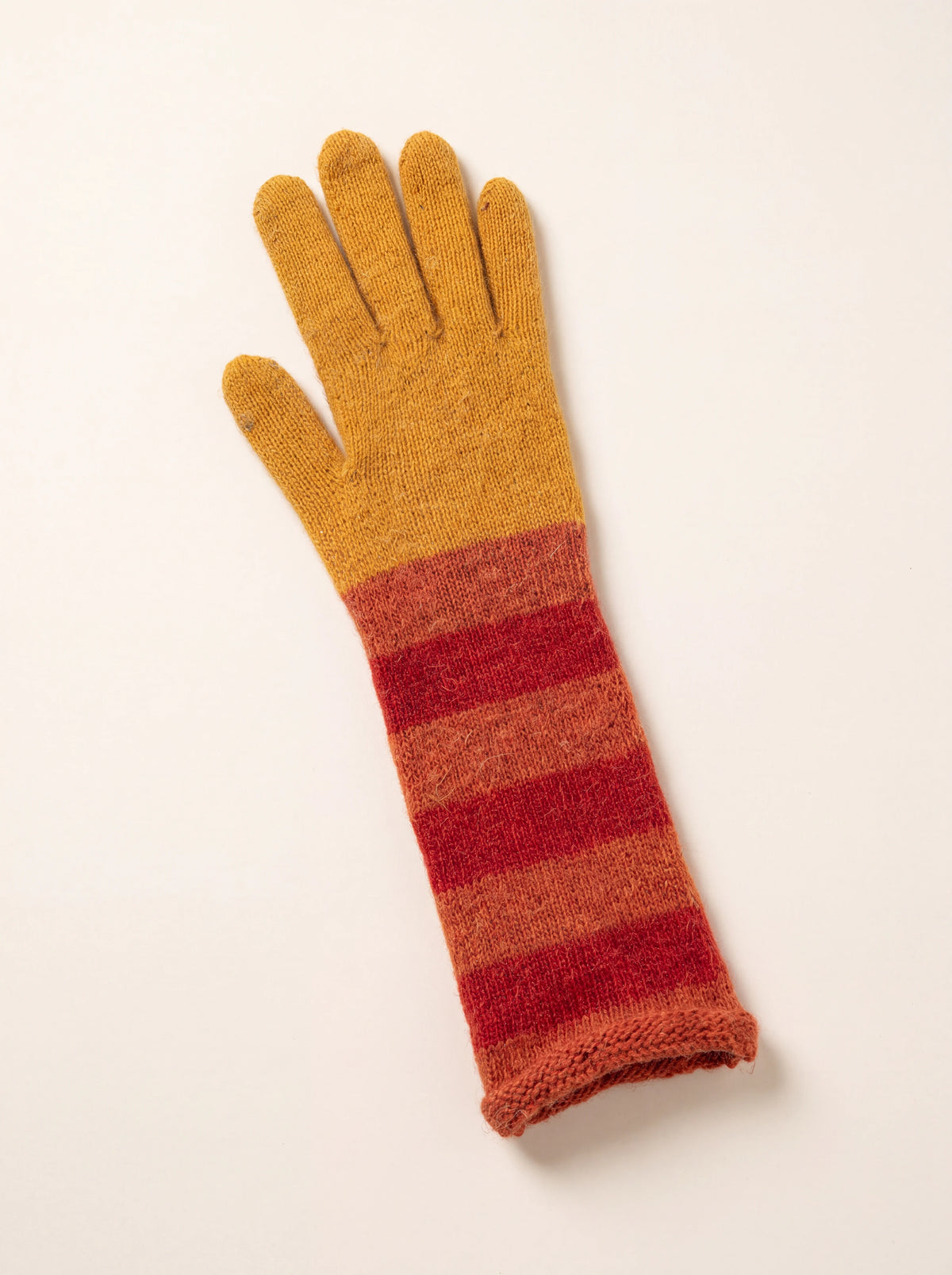 Long knitted glove with a mustard-yellow hand and rust and dark red striped cuff with rolled hem