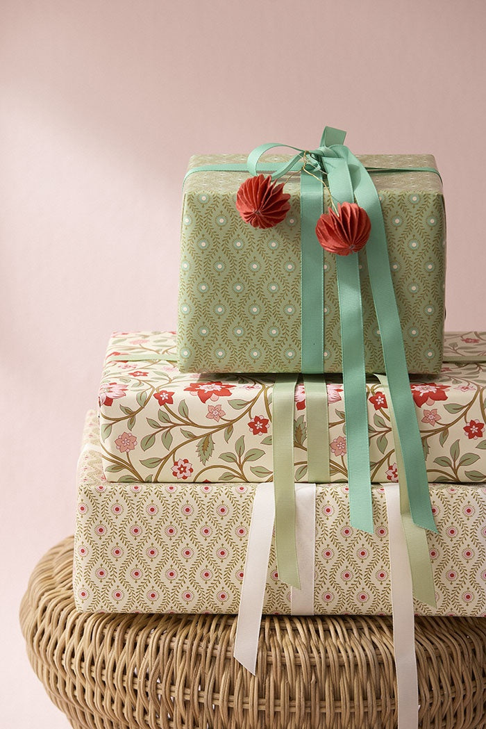 Gift box wrapped in the sage green paper, tied with a ribbon and stacked atop other presents