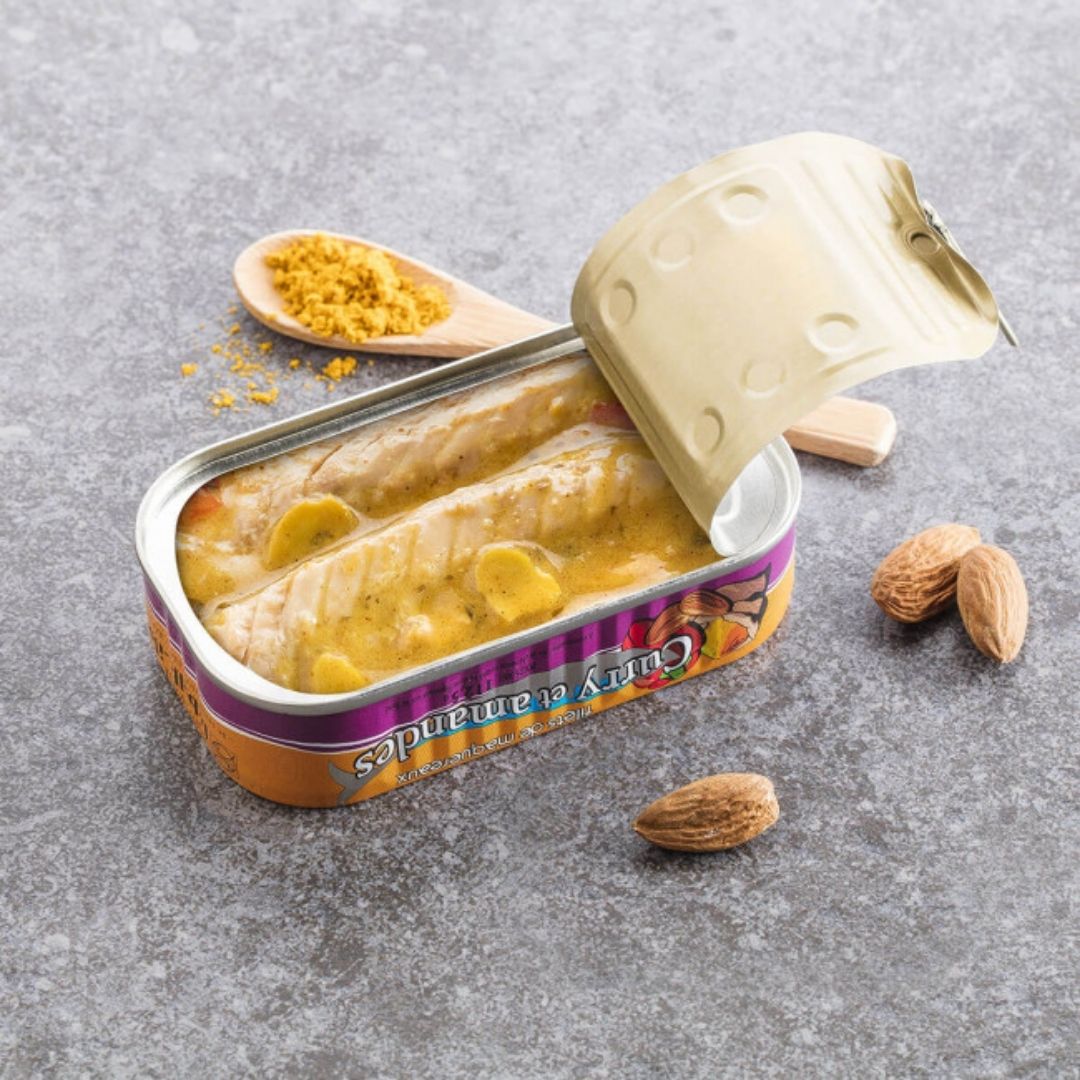 Opened tin of mackerel fillets in yellow curry sauce with whole almonds and ground spices nearby
